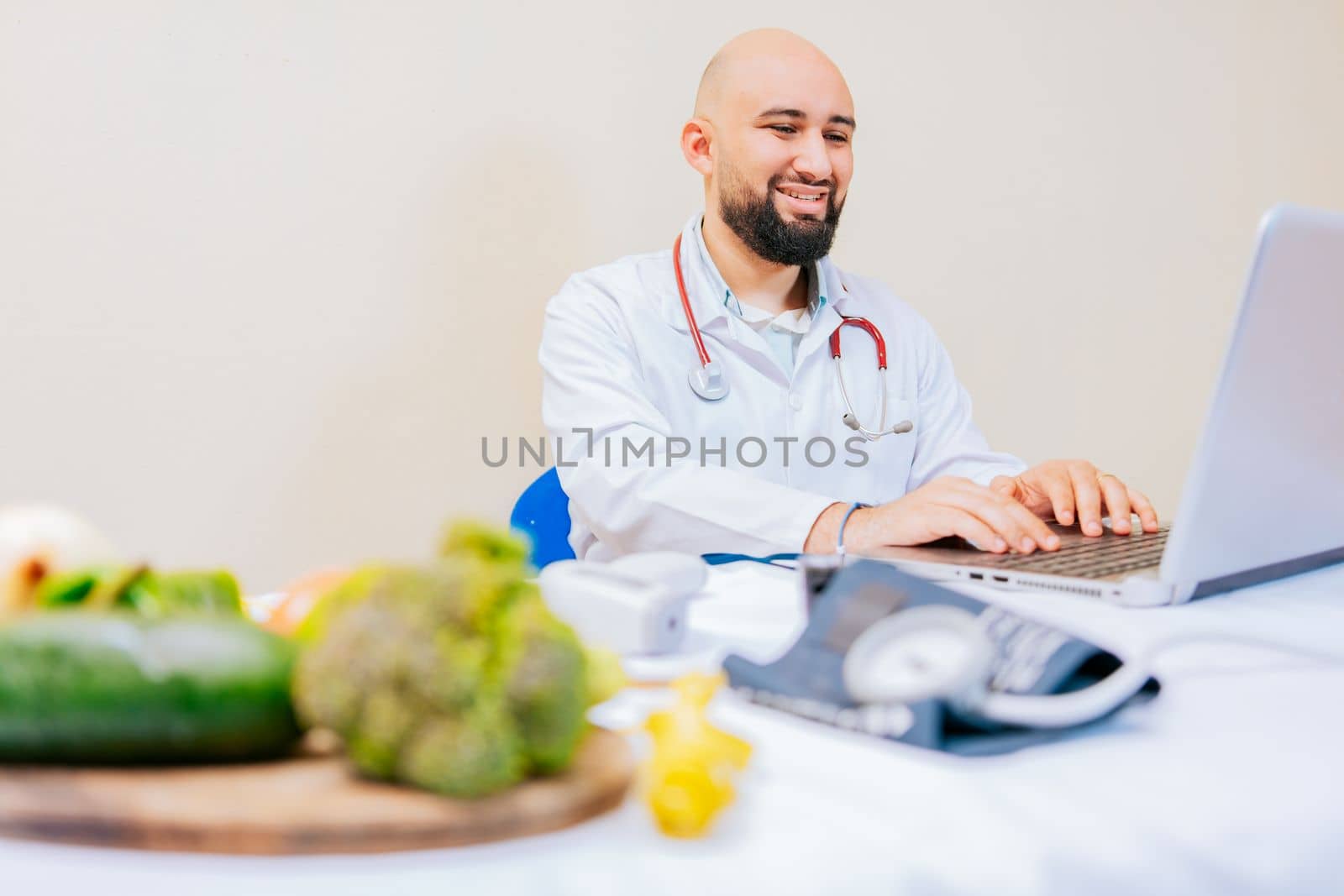 Smiling nutritionist with laptop at desk. Nutritionist doctor using laptop at workplace. Bearded nutritionist doctor working on laptop at desk.