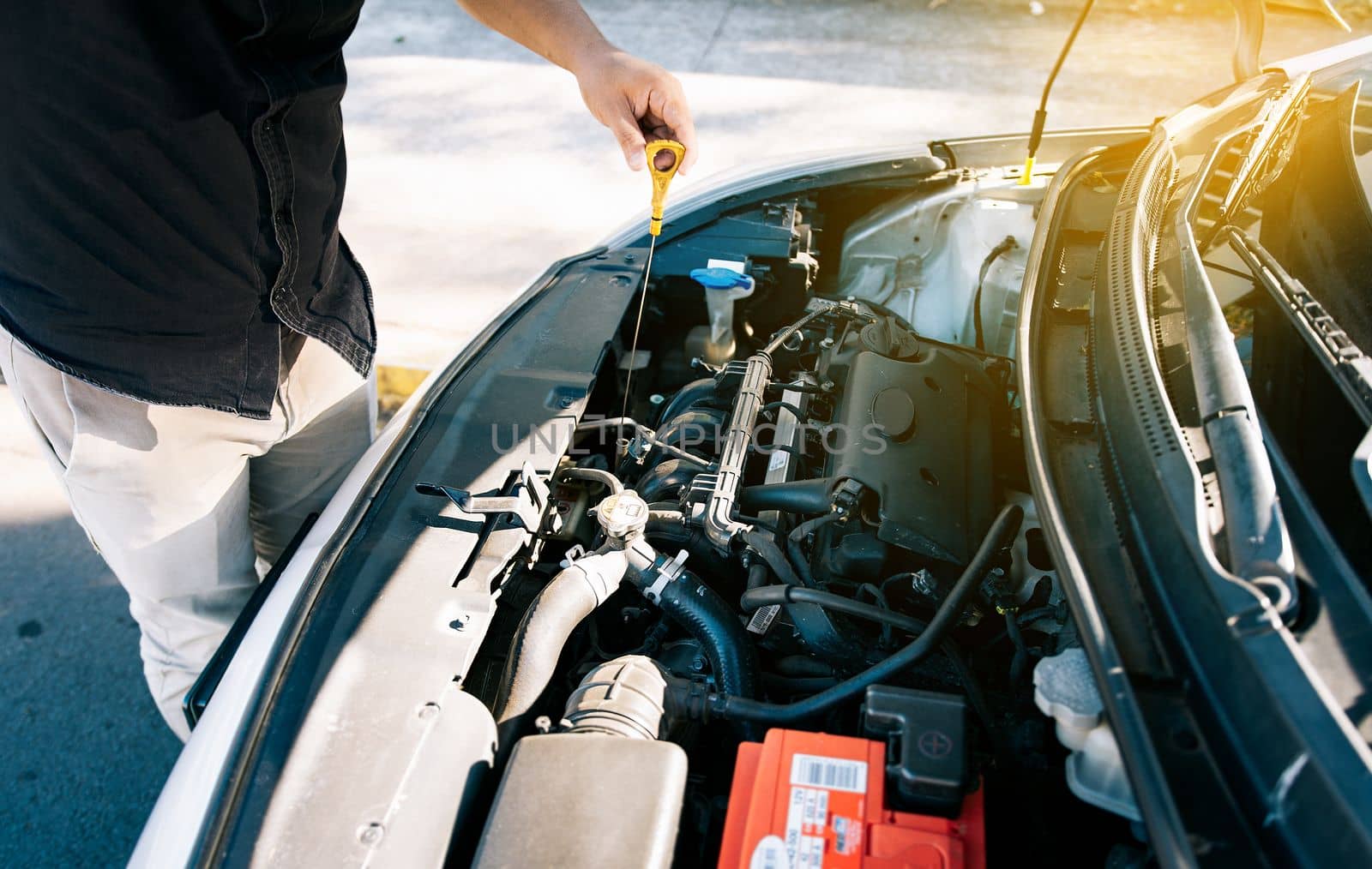 Person checking the oil level of his car in the street. Driver inspecting car oil level, Man checking the oil in his vehicle