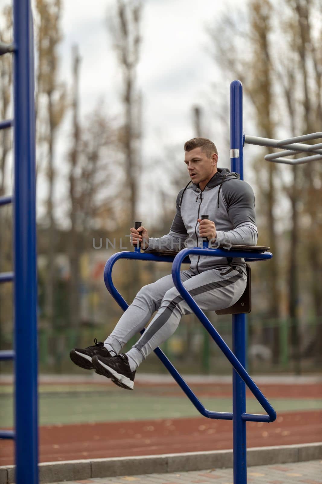 Athletic handsome man doing hanging leg raise at outdoor sports ground