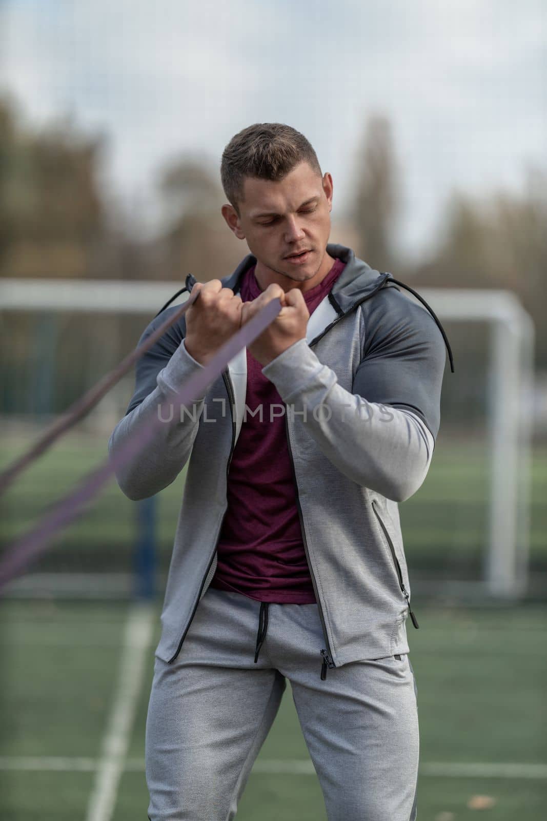 Handsome athletic man exercising with resistance band outdoors in the sun