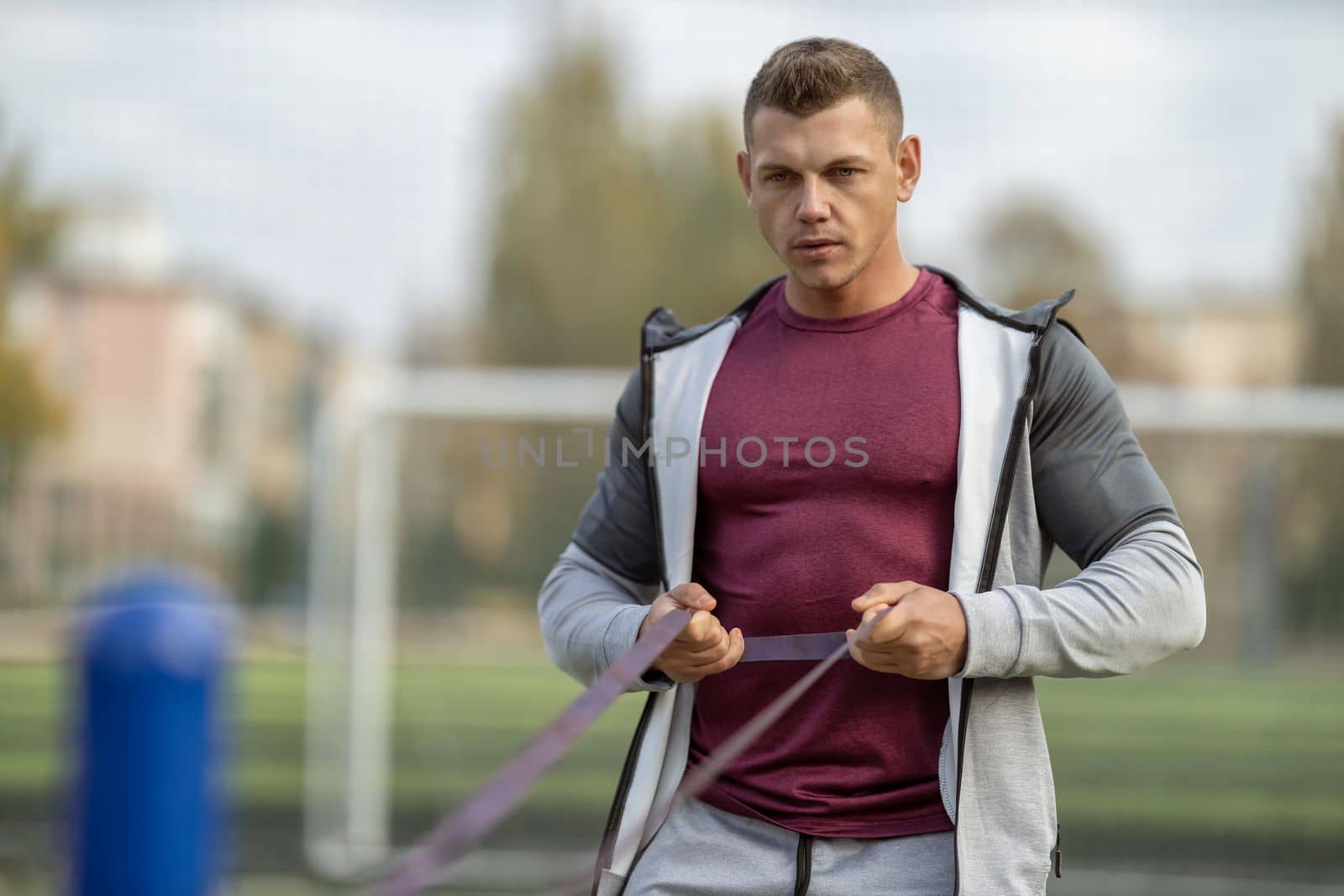 Handsome athletic man exercising with resistance band outdoors in the sun