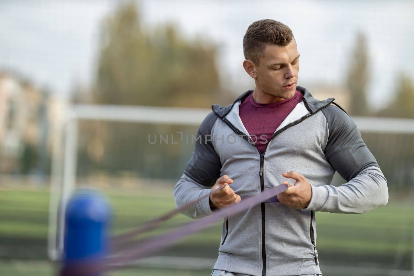 Handsome athletic man exercising with resistance band outdoors in the sun