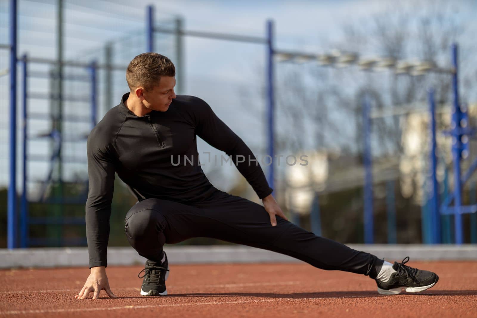 Male runner doing stretching exercises, getting ready for morning workout at outdoor sports ground