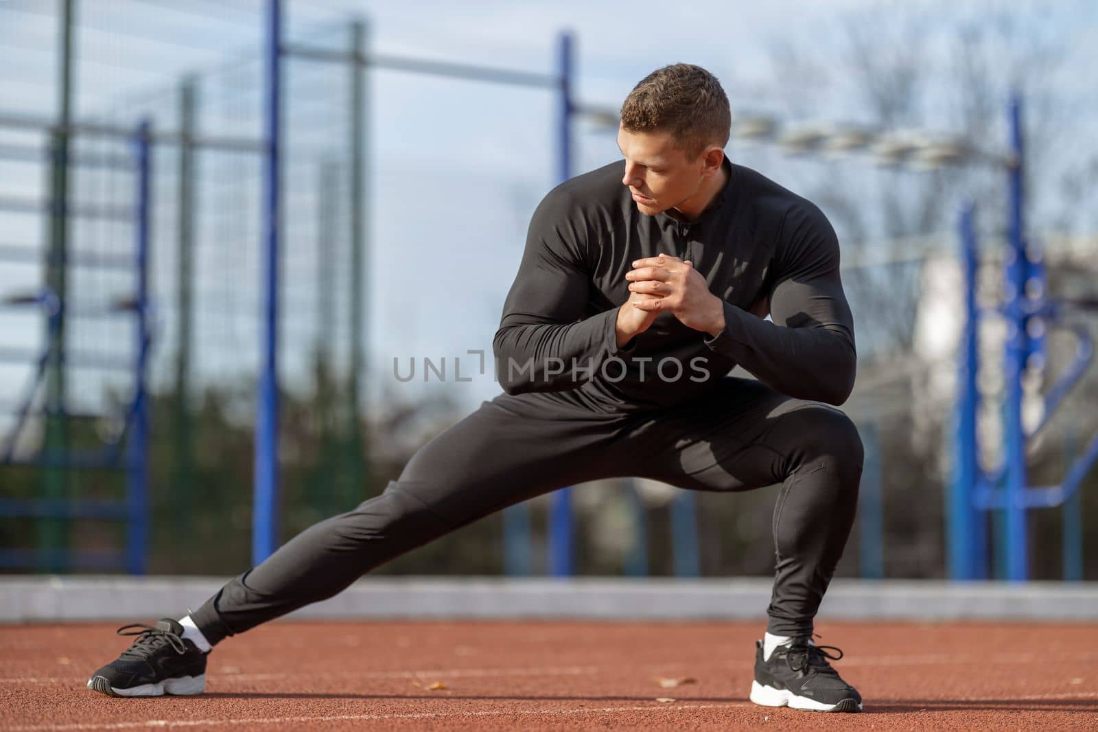 Male runner doing stretching exercises, getting ready for morning workout at outdoor sports ground