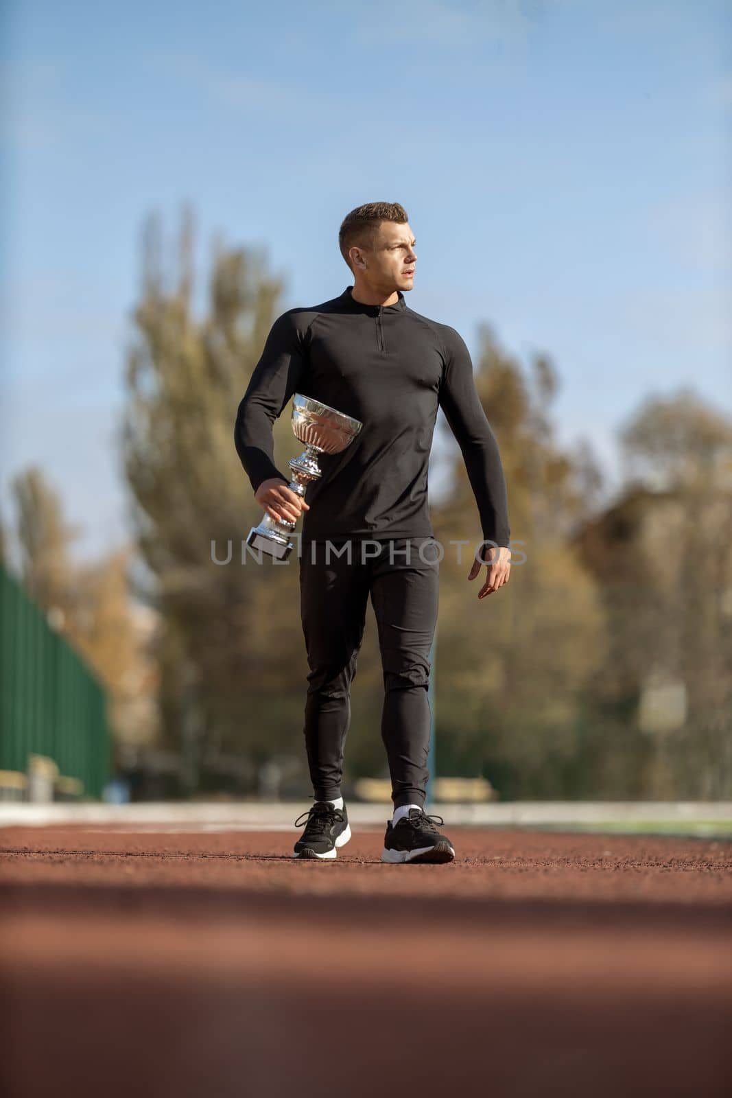 Athletic man in black sportswear at football stadium with champion cup