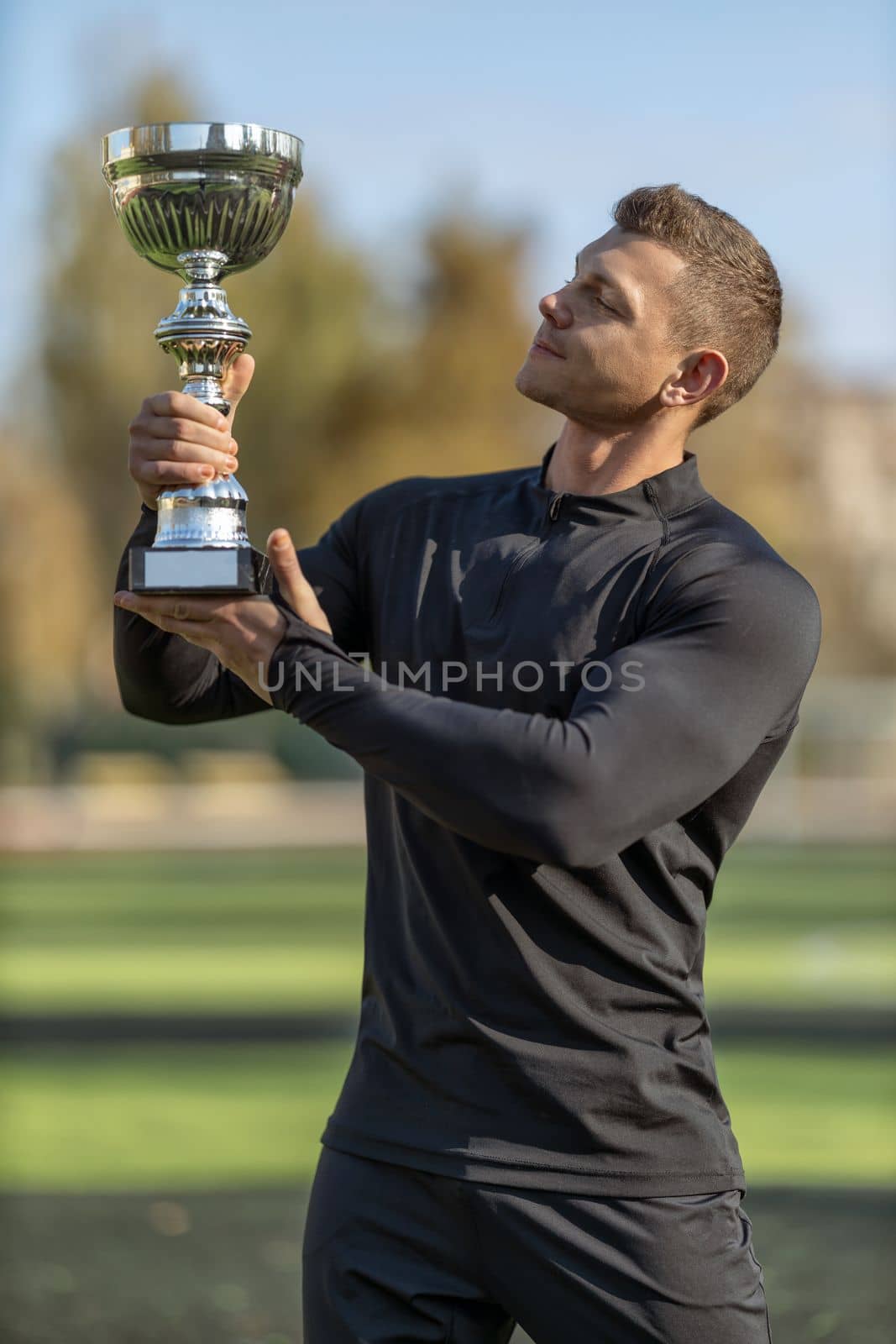 Athletic man in black sportswear at football stadium with champion cup