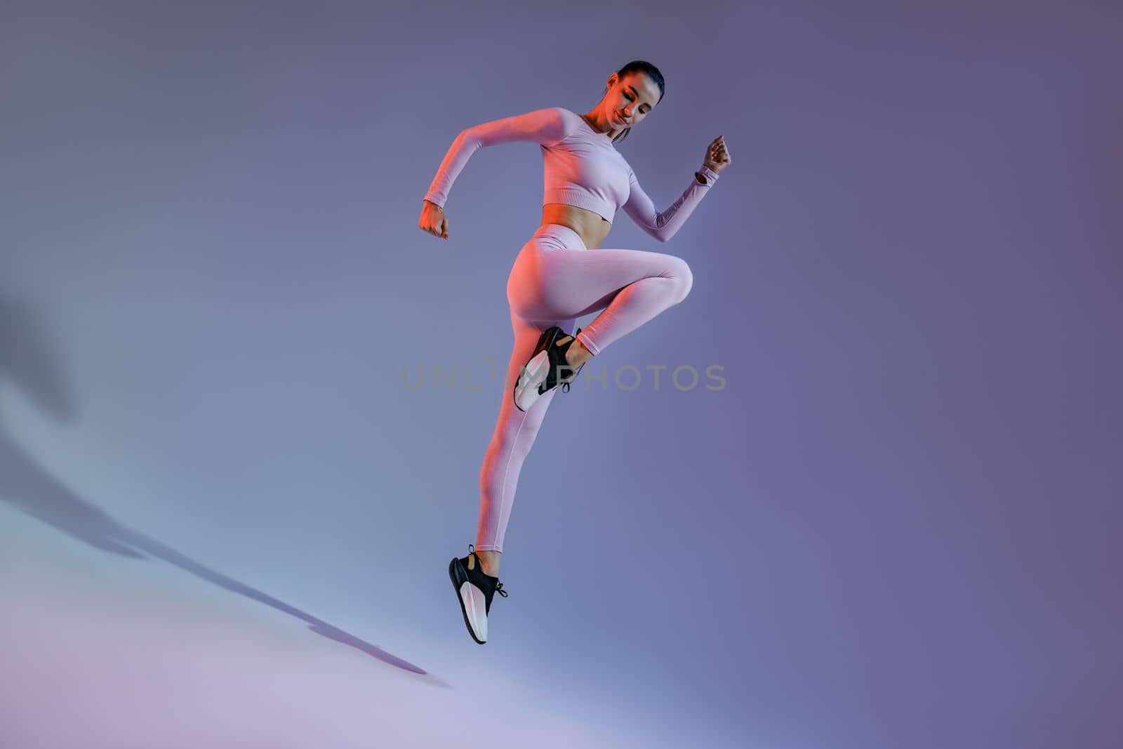 Athletic active woman jumping on studio background with colored filter. Dynamic movement