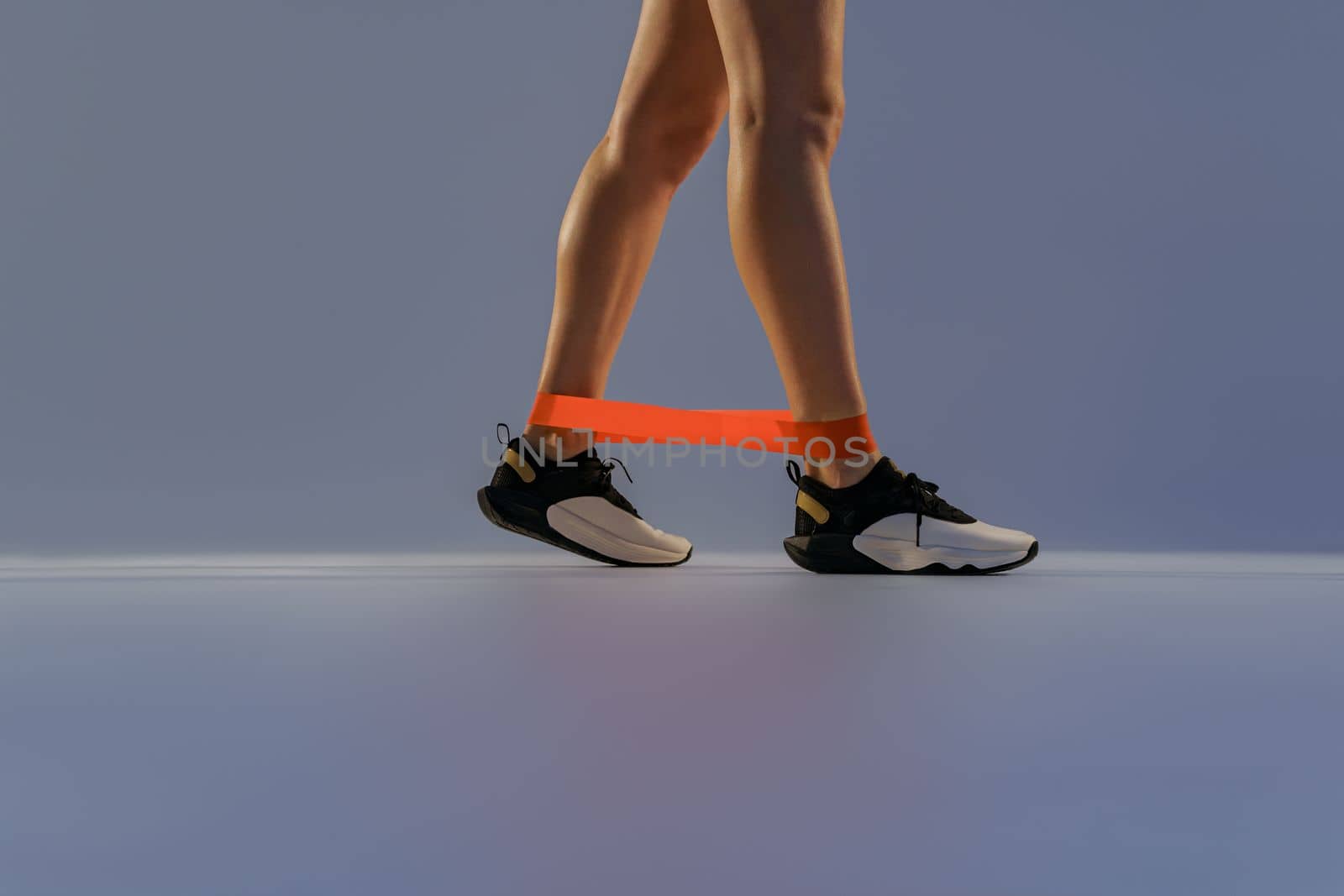 Close up of woman trains legs with fitness elastic band on studio background. High quality photo