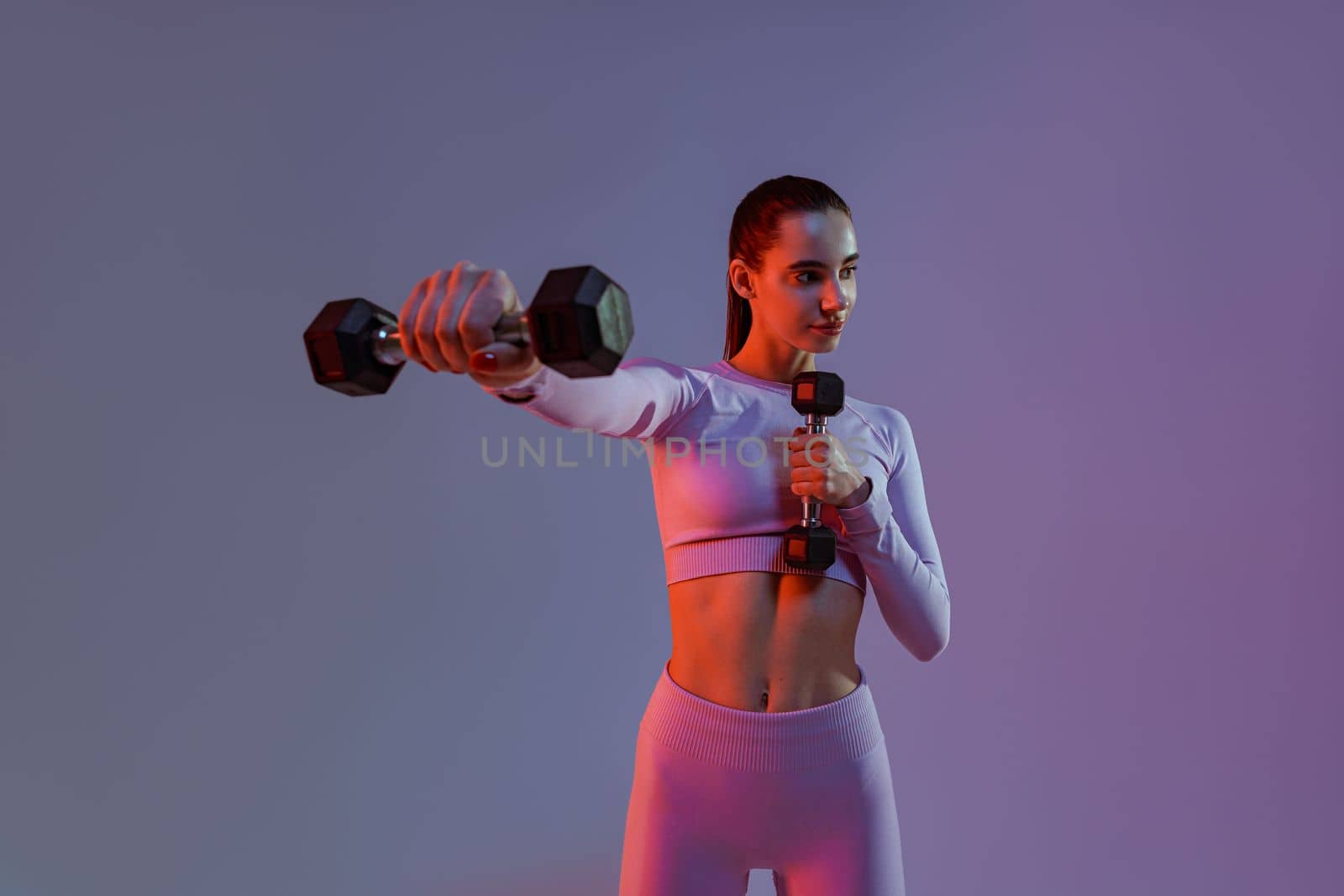 Fitness woman doing exercises with dumbbells on studio background. Strength and motivation by Yaroslav_astakhov
