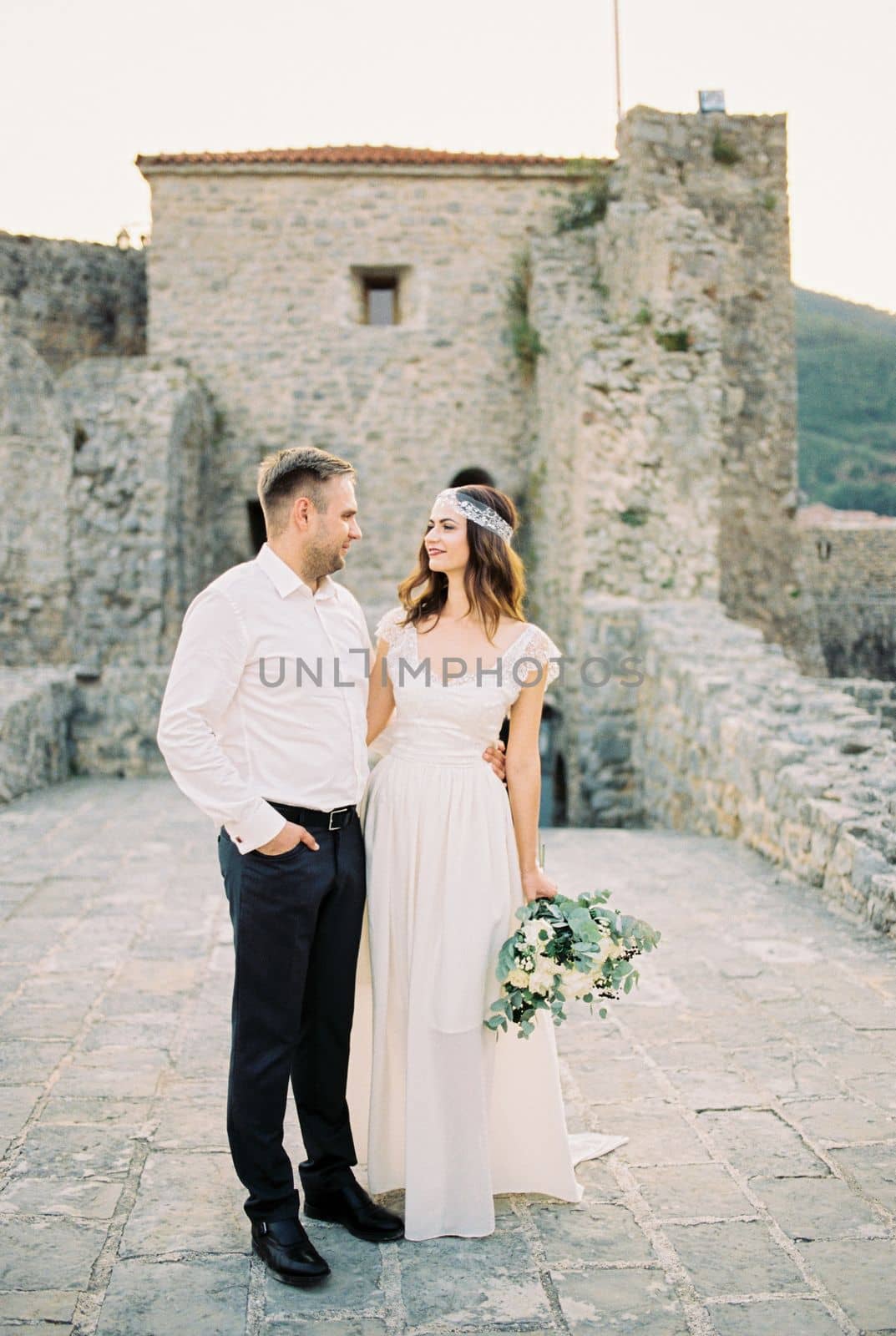 Bride and groom stand embracing on the bridge near the ruins of the old fortress. High quality photo