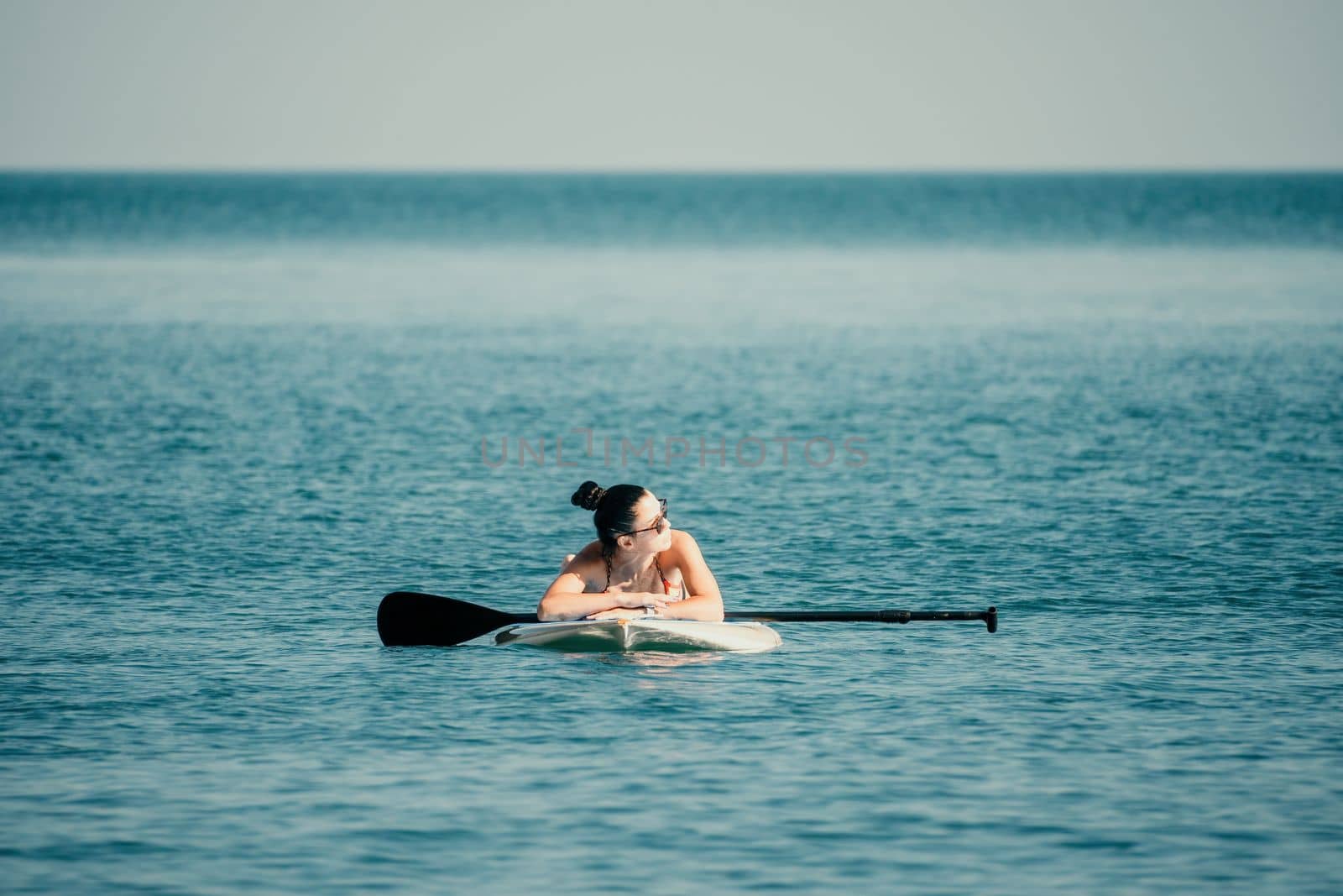 Sea woman sup. Silhouette of happy middle aged woman in rainbow bikini, surfing on SUP board, confident paddling through water surface. Idyllic sunset. Active lifestyle at sea or river