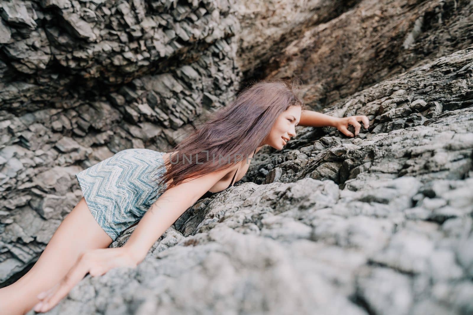 A girl climbs a rock. The athlete trains in nature. Woman overcomes difficult climbing route. Extreme hobby. Tourist woman rock climber hiking on mountains rocks over beautiful sea coast