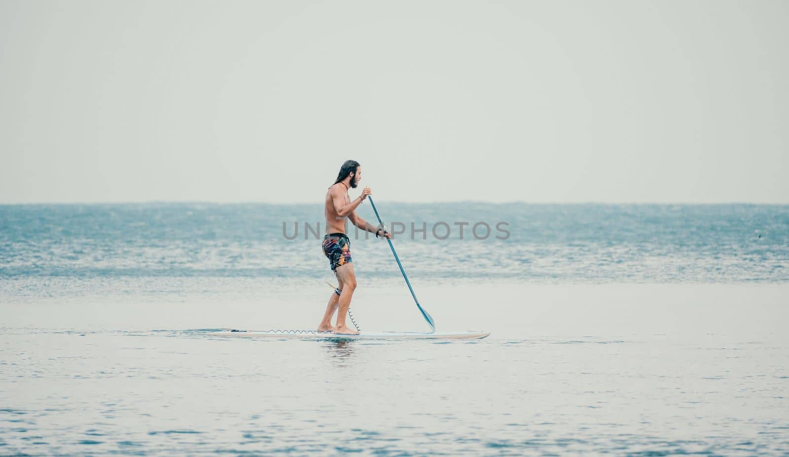 Asian man swimming in sea water and paddleboarding passing beautiful sea at summer sunset. Healthy strong male enjoy outdoor active lifestyle and water sports on holiday vacation