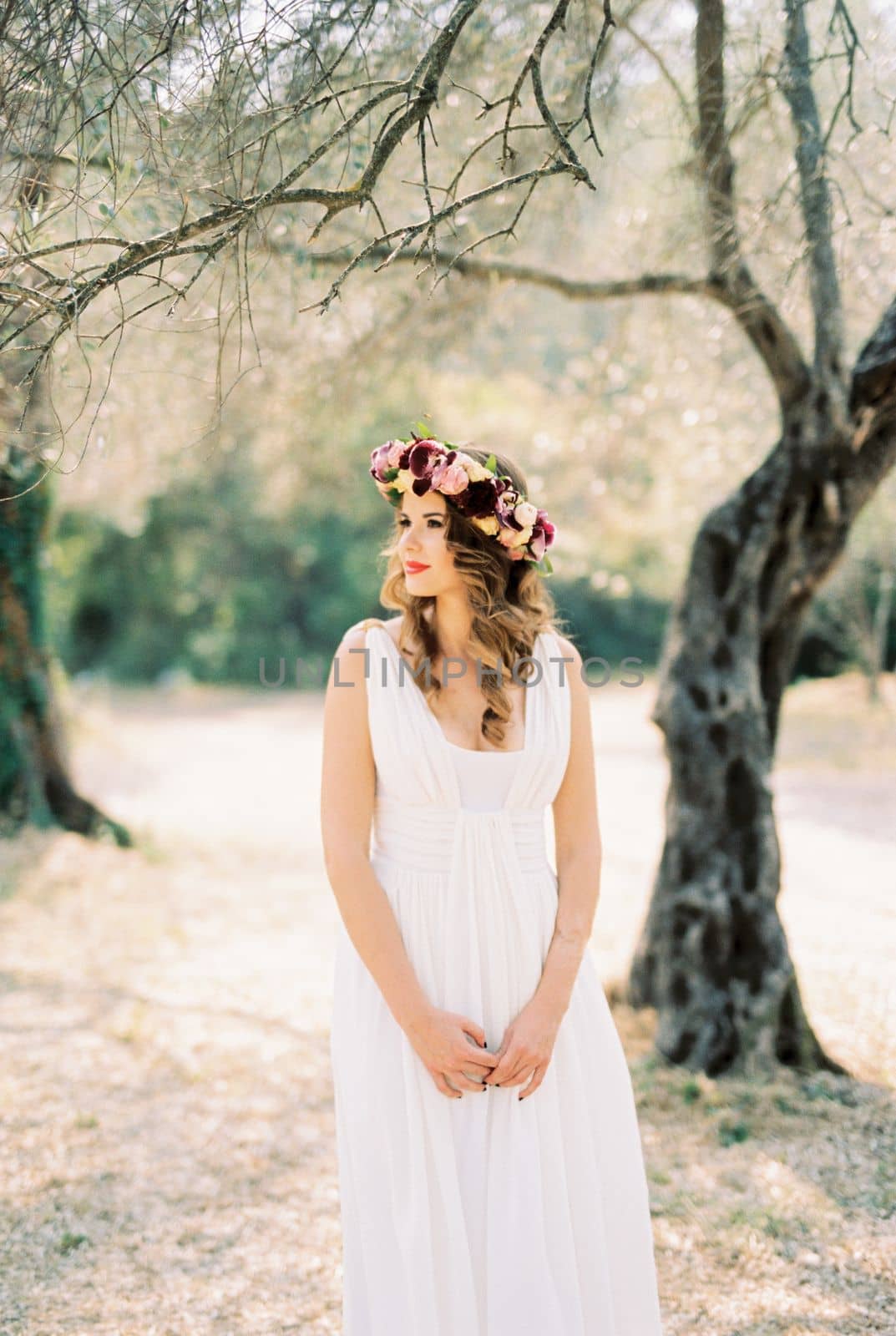 Bride in a toga dress with a wreath stands under a tree in the park. High quality photo
