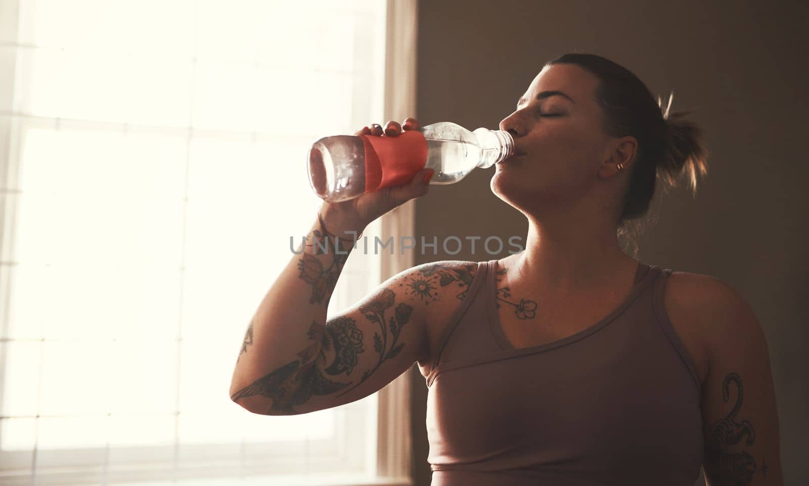Its vital to drink water before, during and after exercise. a young woman drinking water after her workout at home