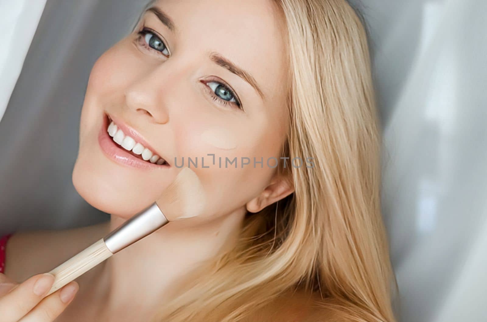 Beautiful blonde woman applying liquid make-up foundation on her skin with make-up brush.
