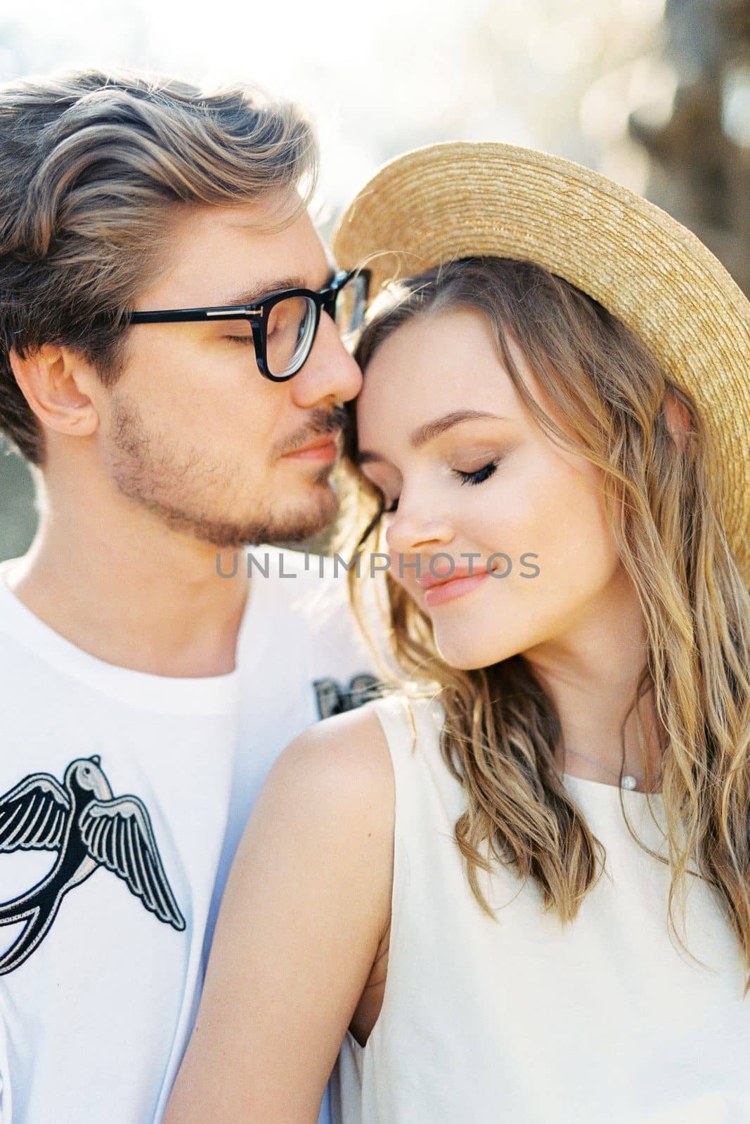 Man in glasses touches the forehead of a woman in a straw hat. Portrait by Nadtochiy