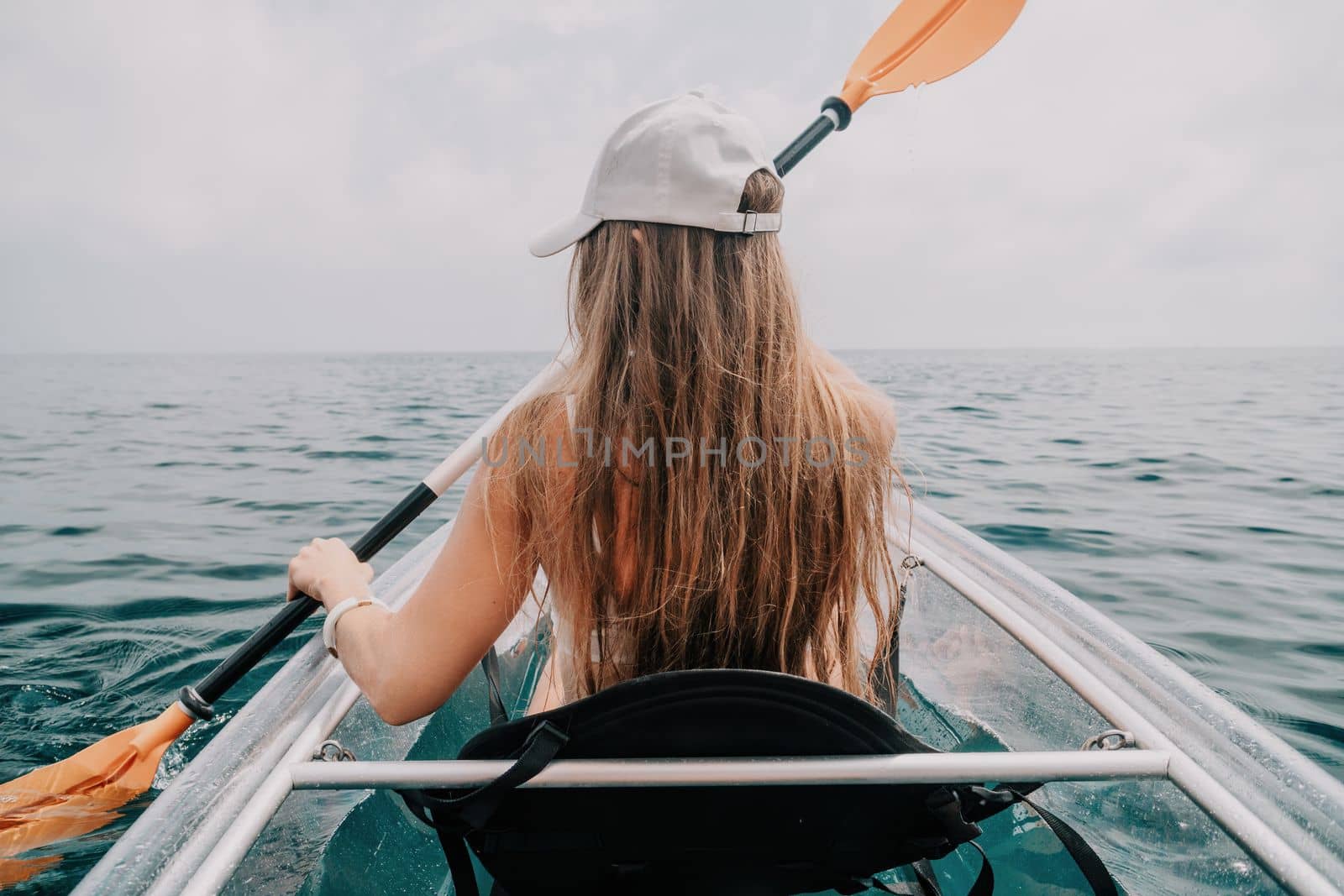 Woman in kayak back view. Happy young woman with long hair floating in transparent kayak on the crystal clear sea. Summer holiday vacation and cheerful female people having fun on the boat.