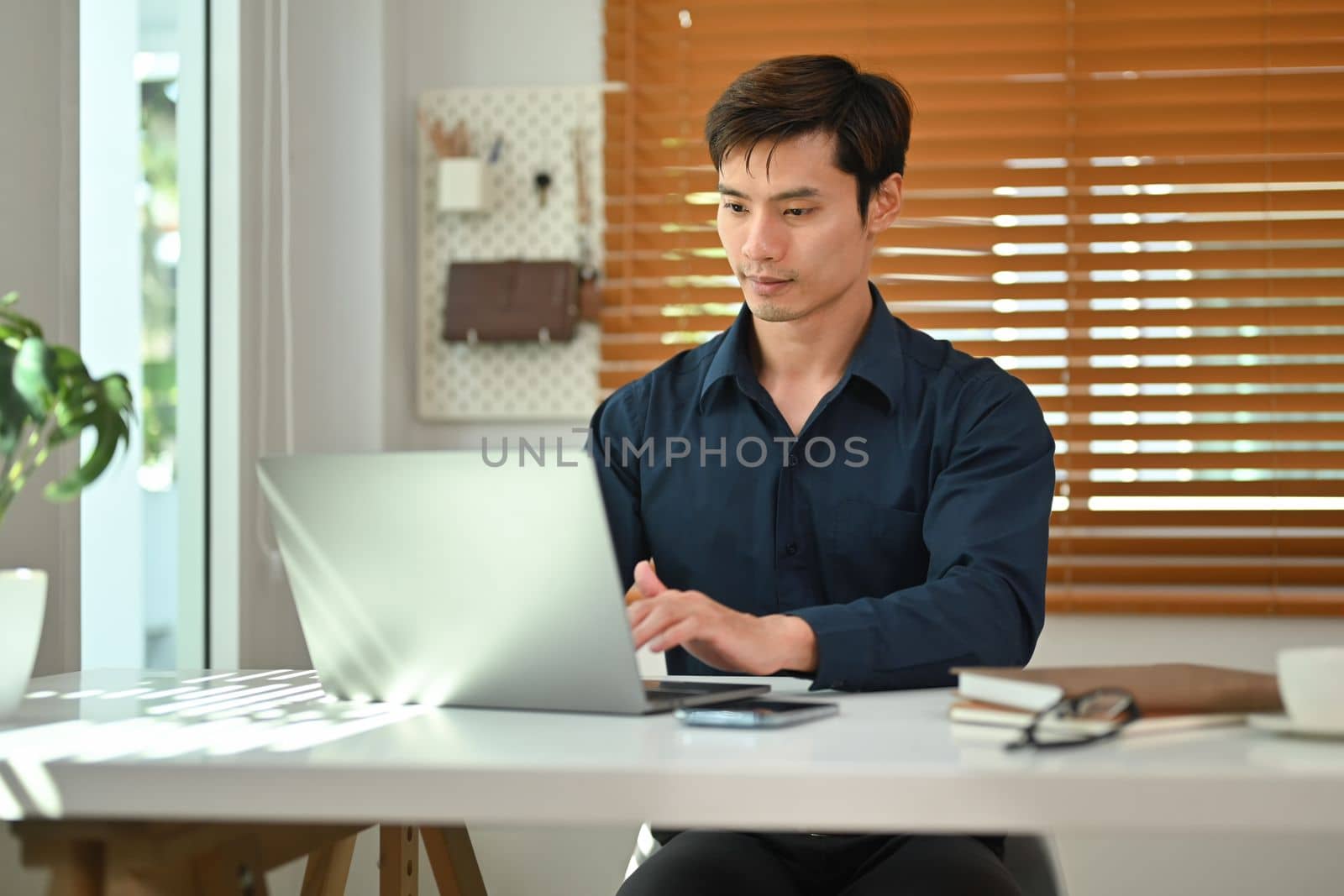 Handsome businessman using laptop computer working at home office. Remote job, technology and lifestyle concept by prathanchorruangsak