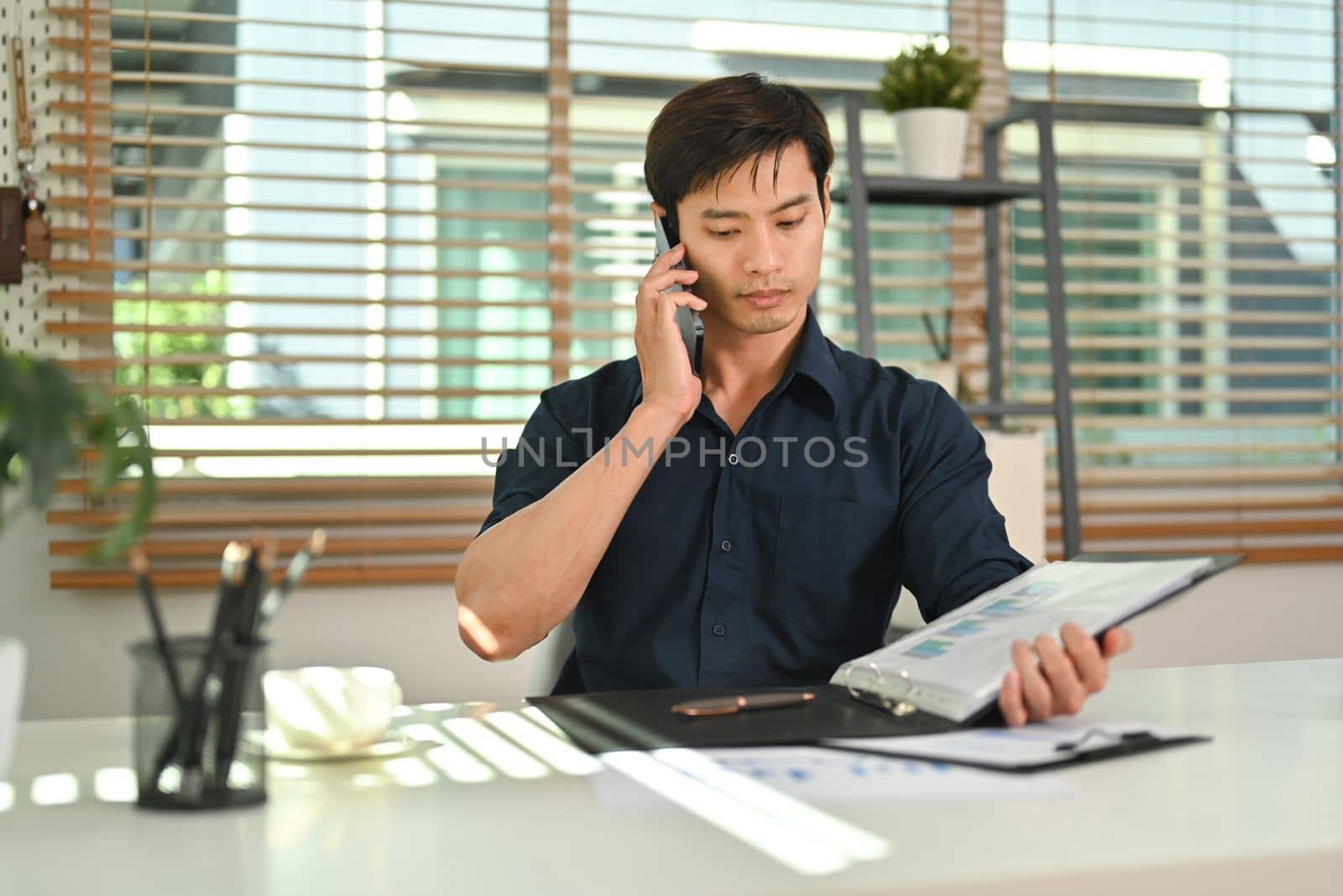 Attractive asian man having phone conversation while working remotely from home by prathanchorruangsak