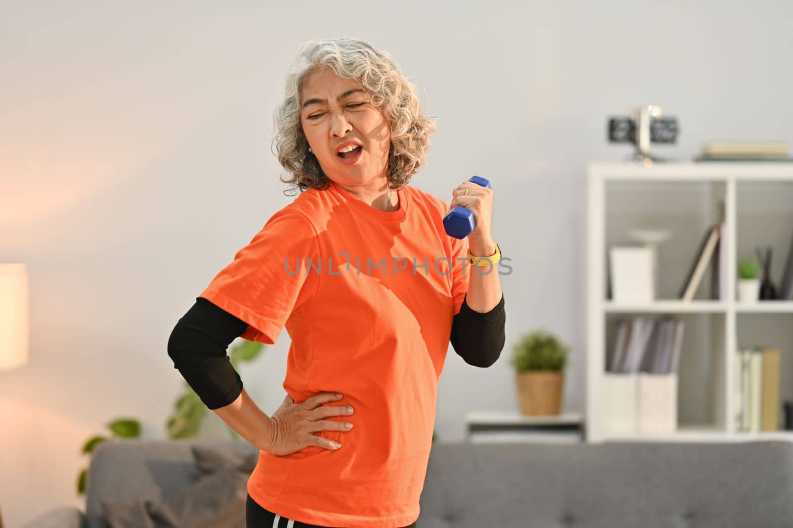 Active middle aged woman in sport clothes exercising with dumbbells in living room. Healthy active lifestyle concept.