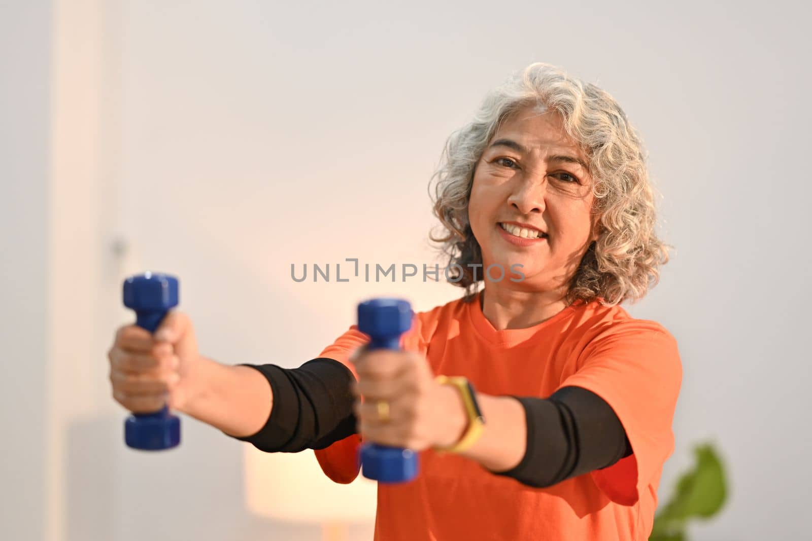 Active middle aged woman womanexercising with dumbbells at home. Retirement, healthy lifestyle concept by prathanchorruangsak