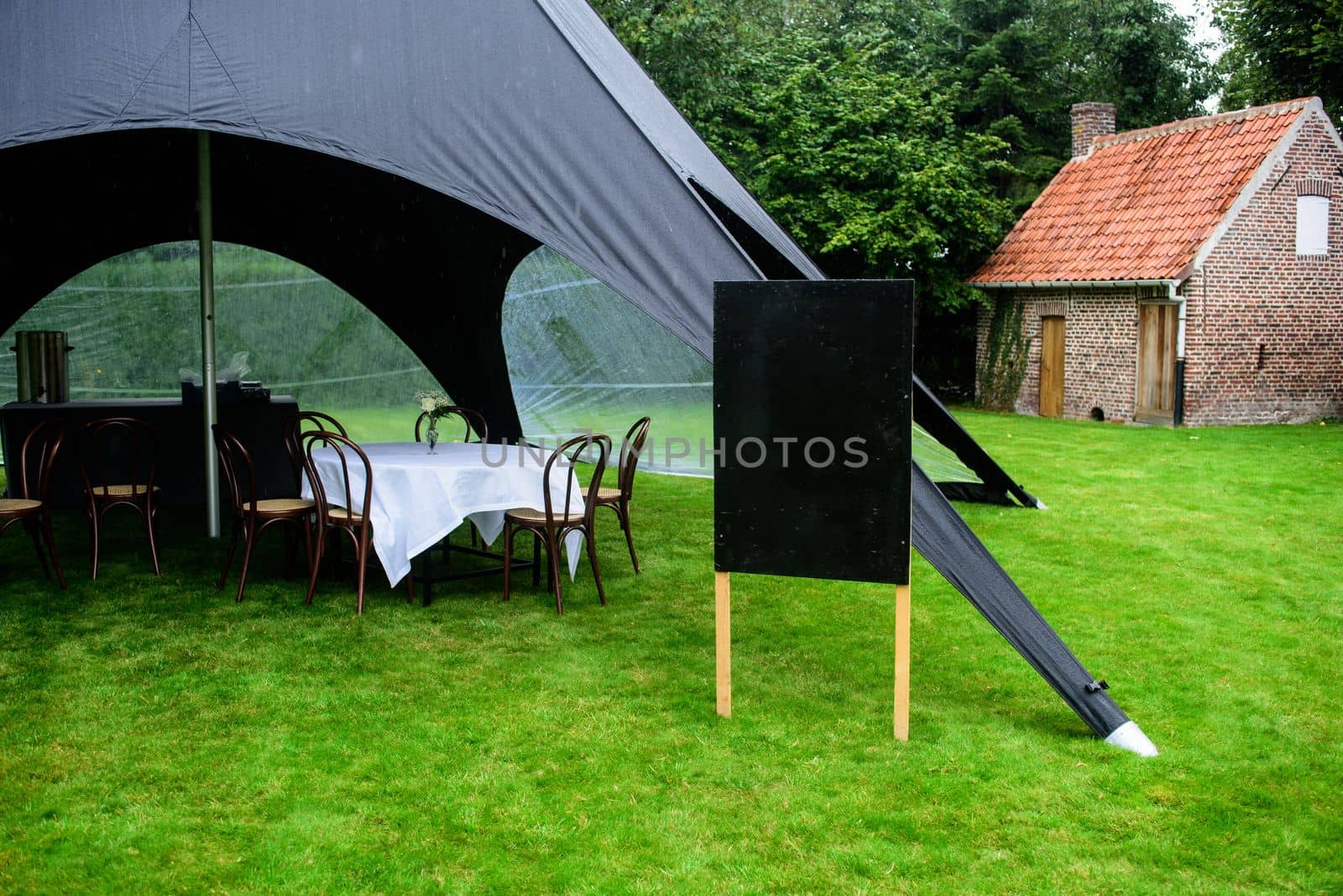 black tent in a garden with dressed tables waiting for people and a black board to writing something on it