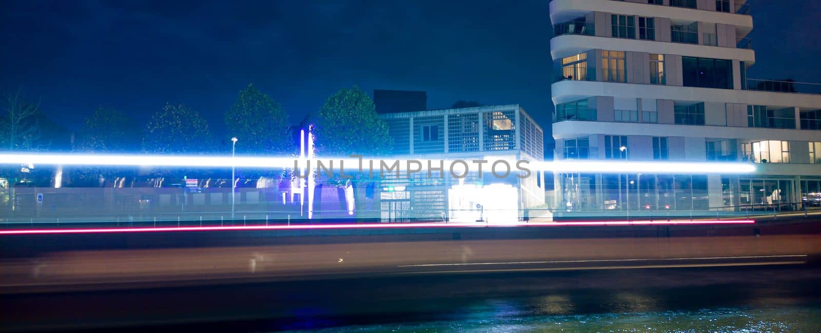 Lighttrails of a boat passing at night throug a city with some buildings in the background