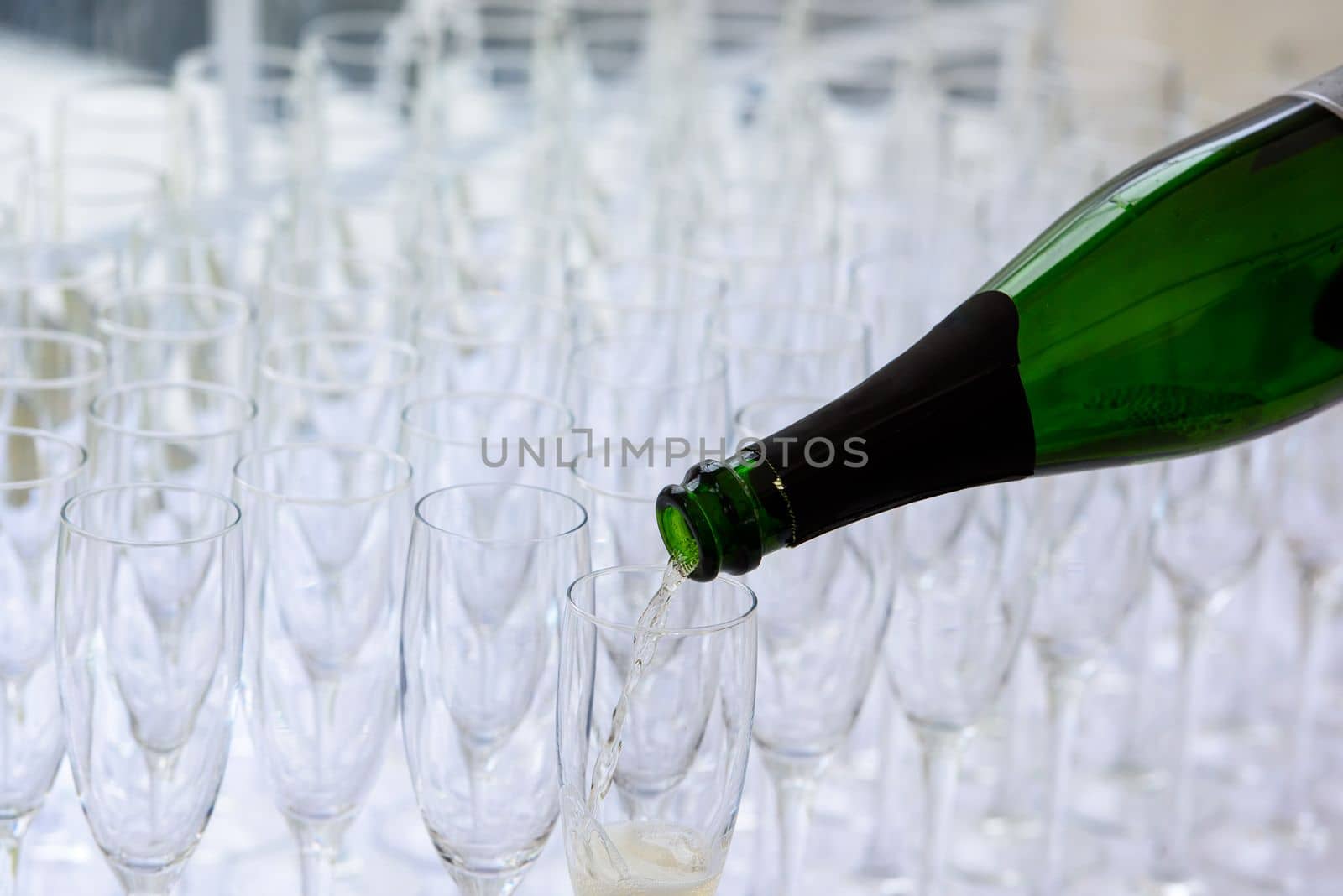 closeup of a champagne bottle pooring champagne into a champagne flute against a blurred glasses in the background