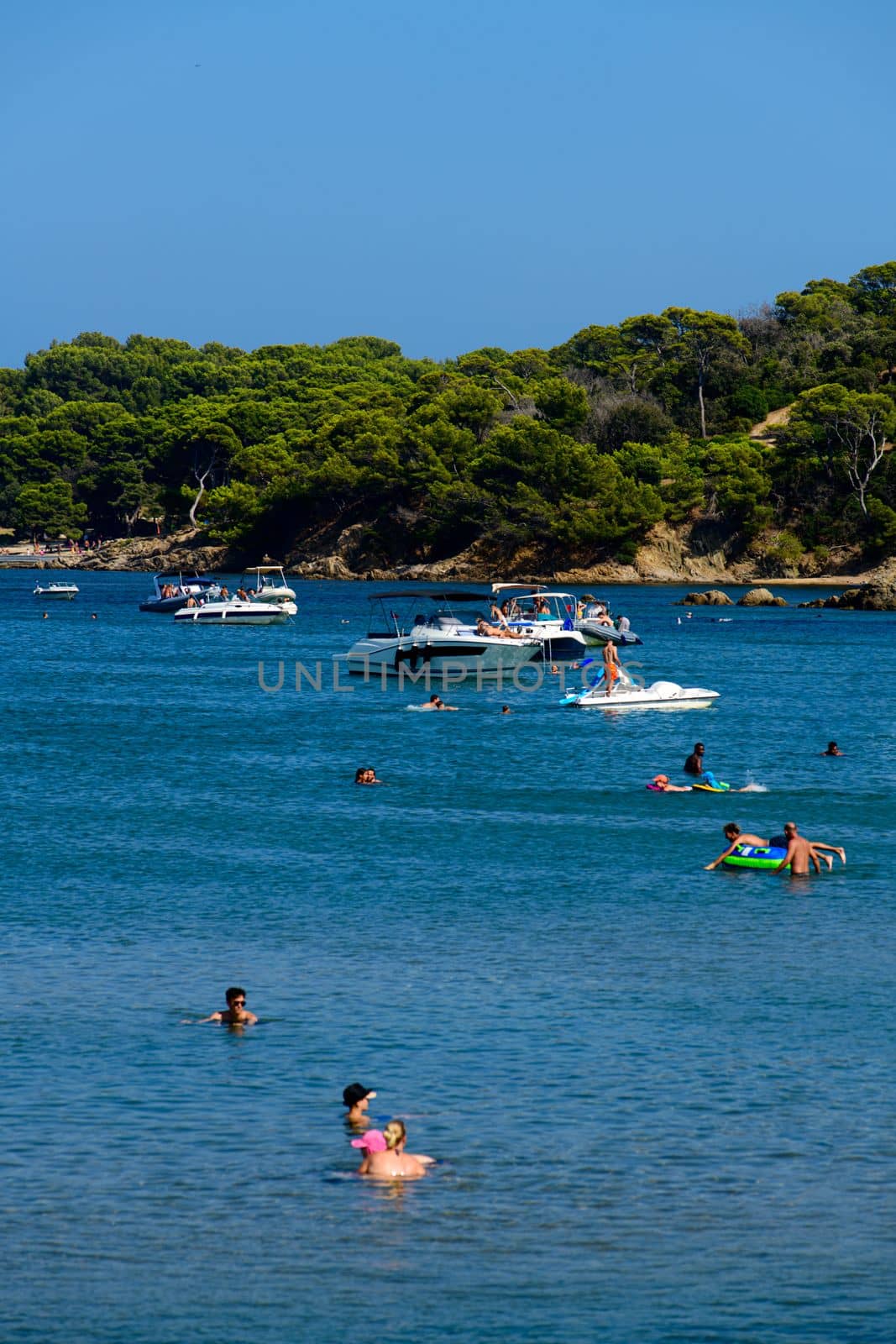 people playing in the mediterranean sea and jumping from boats on a sunny summerday against a rocky coastline