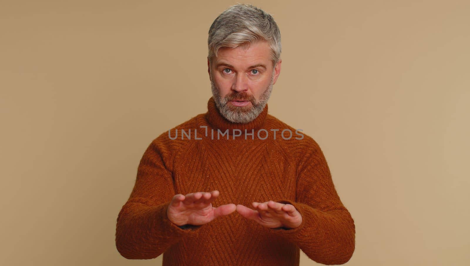 Hey you, be careful. Middle-aged man warning with admonishing finger gesture, saying no, be careful, scolding and giving advice to avoid danger, disapproval sign. Senior mature guy on beige background