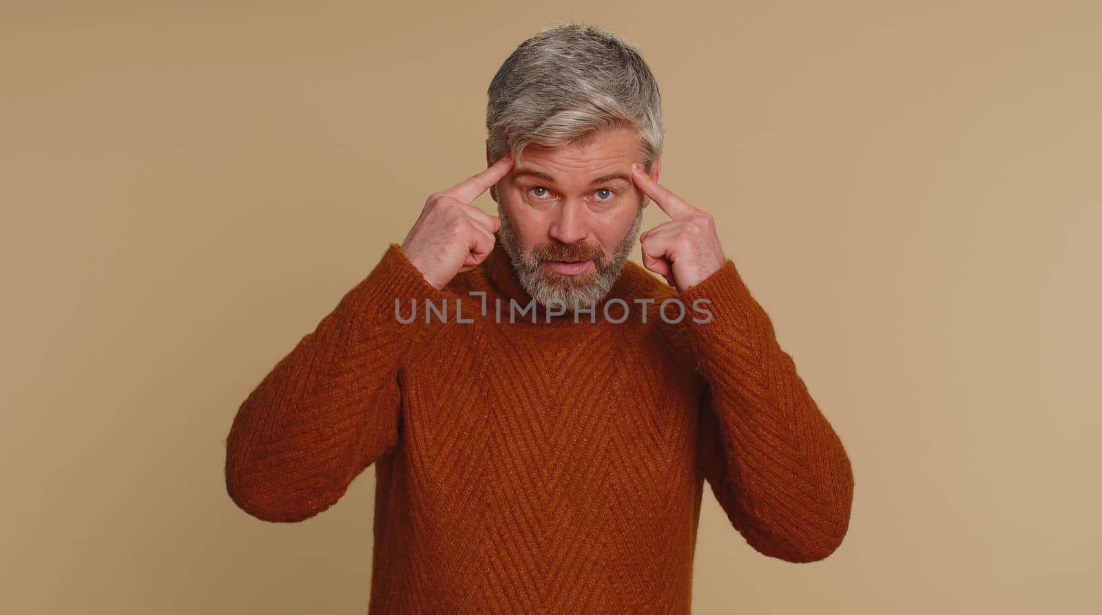 You are crazy, out of mind. Middle-aged elderly old man pointing at camera and showing stupid gesture, blaming some idiot for insane plan. Senior mature guy isolated alone on beige studio background