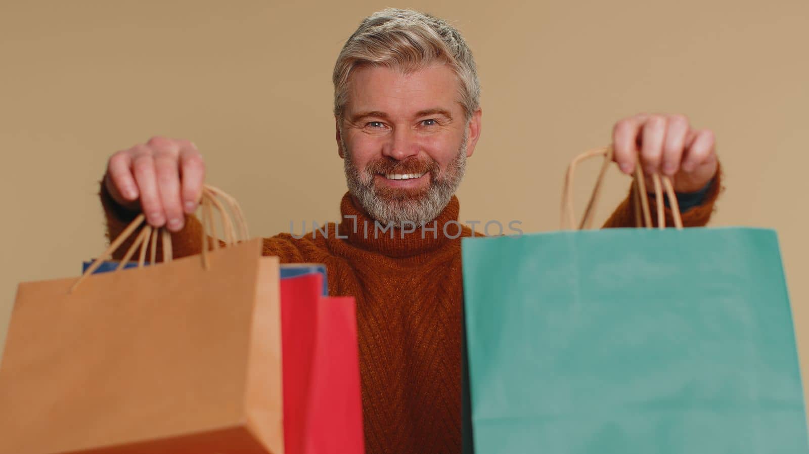 Middle-aged man showing shopping bags, advertising discounts, smiling looking amazed with low prices by efuror