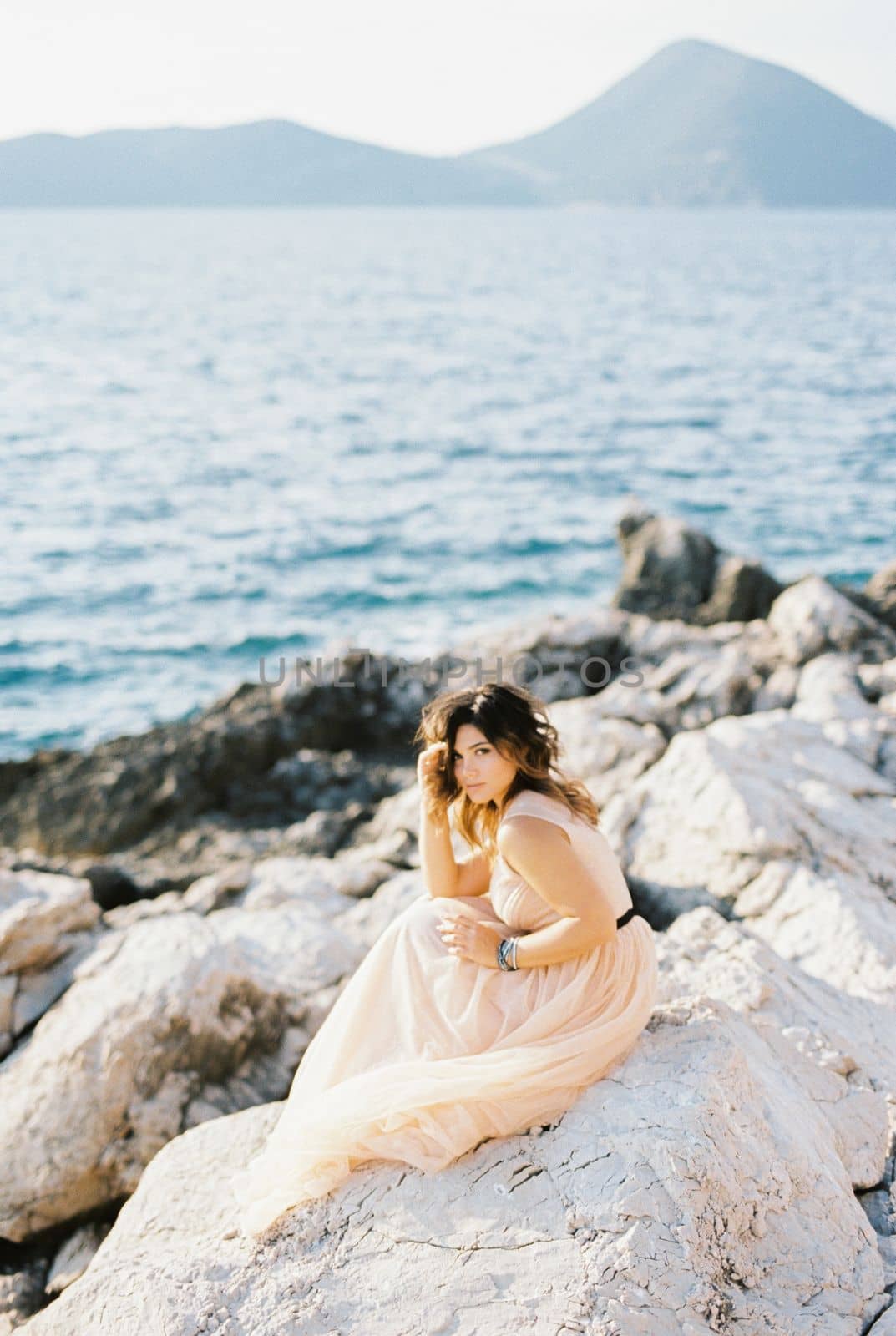 Bride sits on the rocks by the sea with her head propped up by her hand. High quality photo