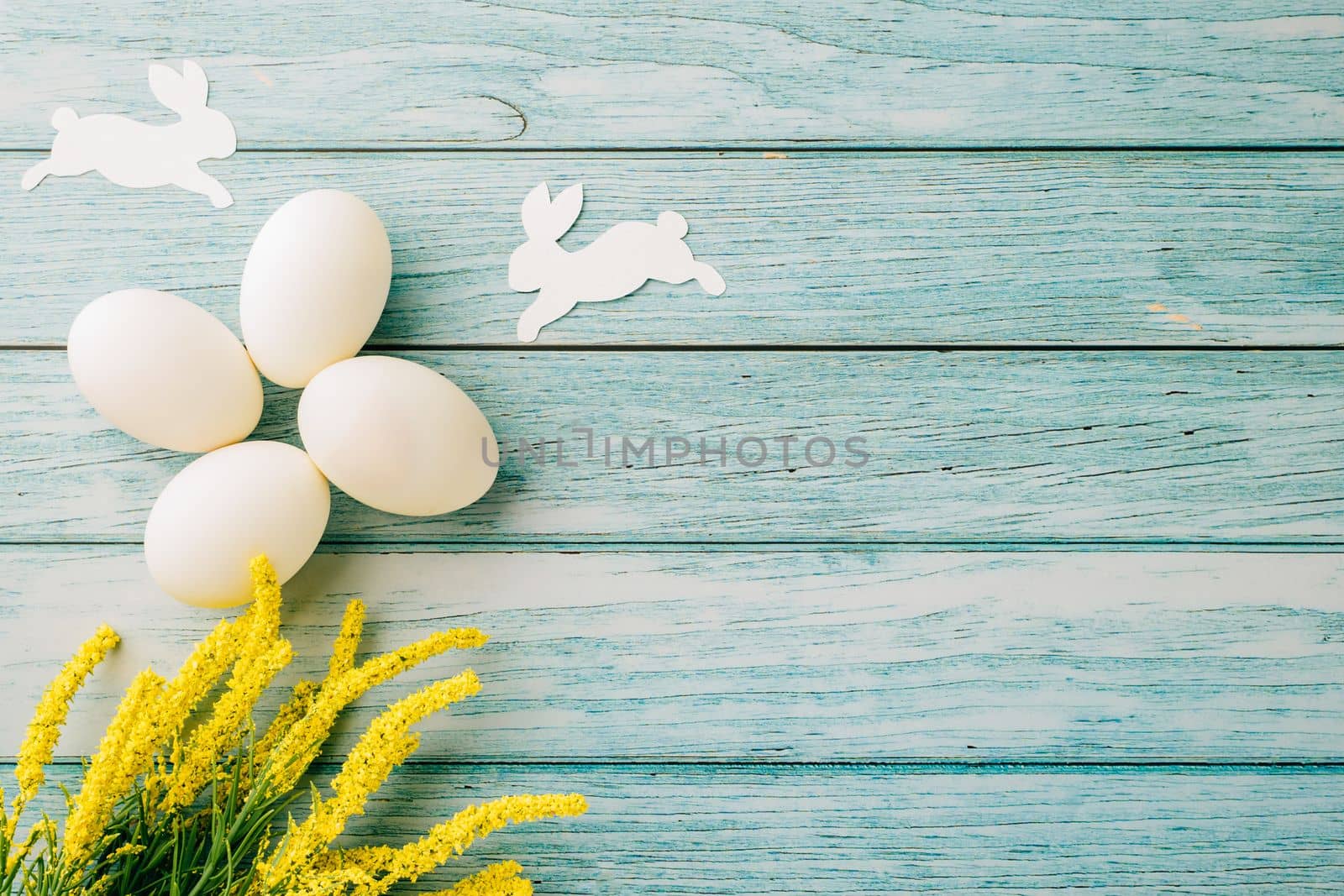 Happy Easter Day Concept. Flat lay of holiday banner background design white easter eggs and beautiful yellow flowers on blue wooden background with empty copy space, celebration greeting card