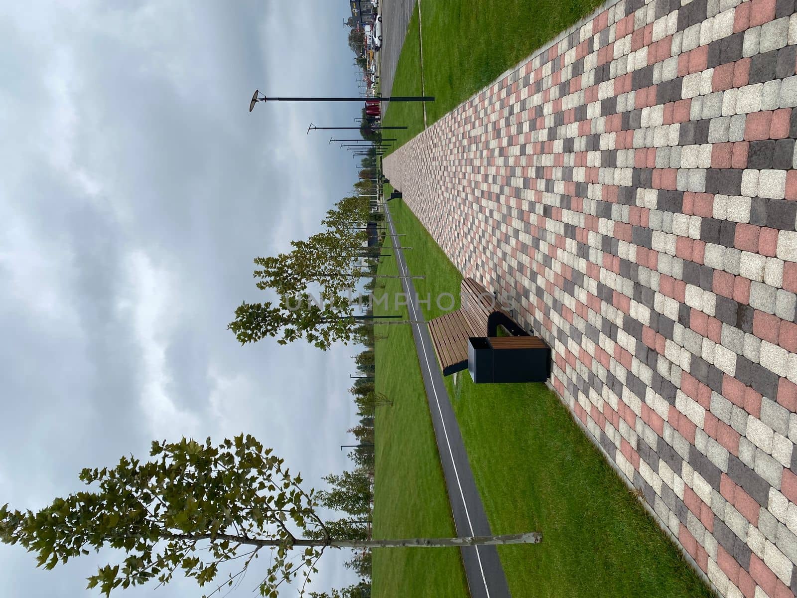 walking path in the park is paved with multi-colored paving stones. Bench and trash can next to the sidewalk. Bicycle path in the background. Selective focus. horizontal image by Proxima13