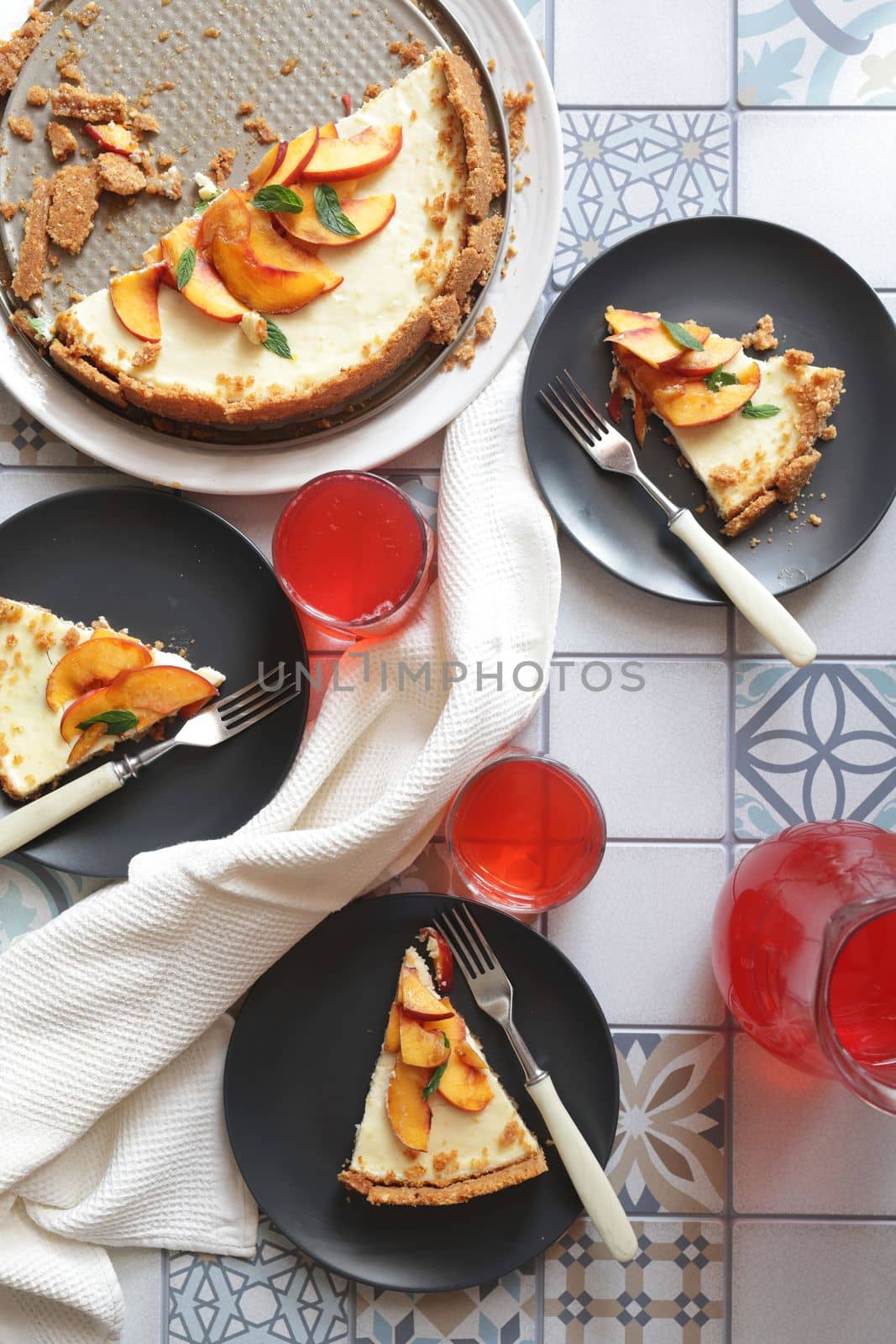 Portions of ginger tart with fresh peach slices on black plates. Tart cut into portions with crumbs. Berry juice in glass glasses by Proxima13