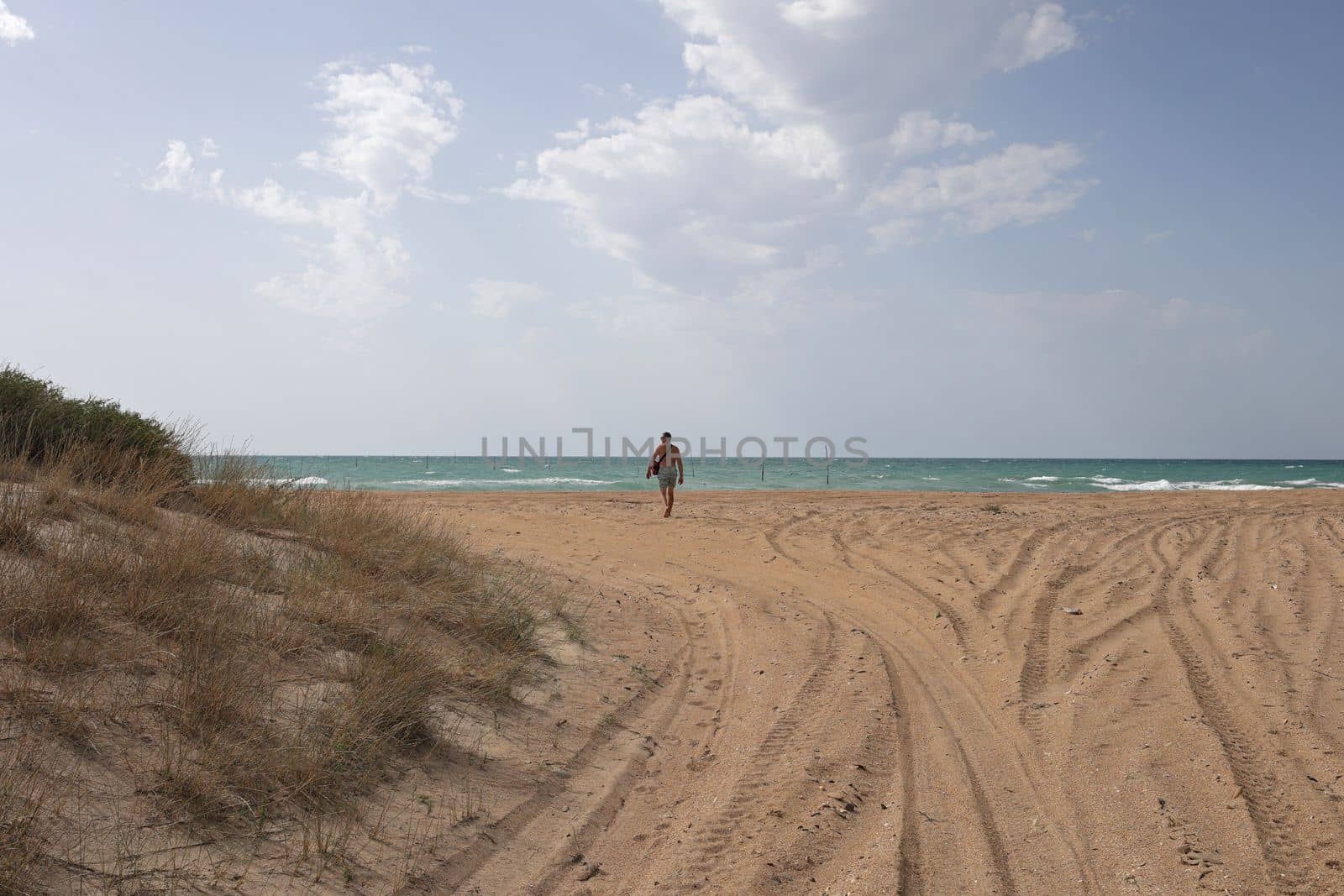 Sea access to the beach. Wide access to the beach with sand and grass. Man walking towards the water towards the beach