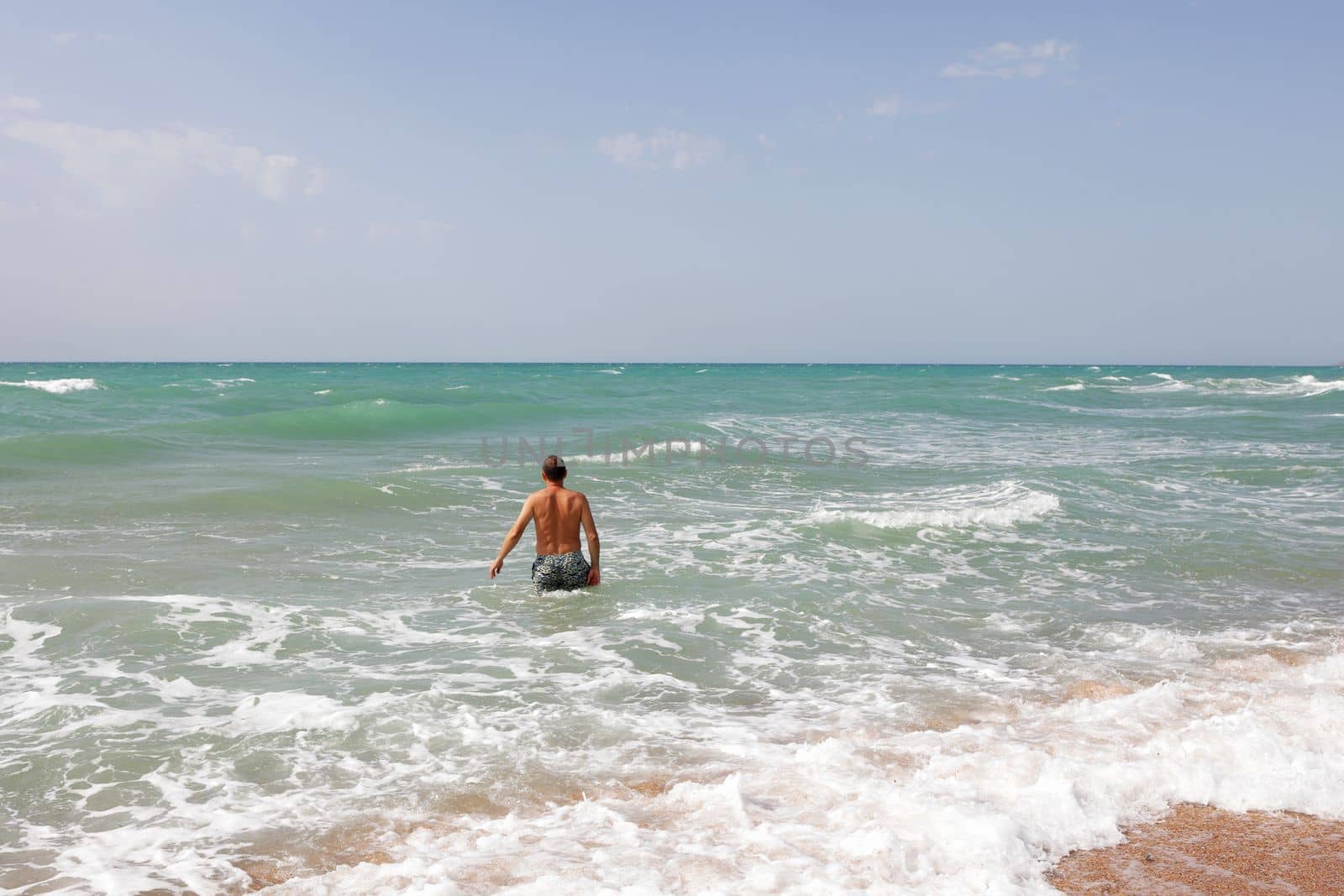 man enters the sea to swim. Moderate waves on the sea, sandy beach.