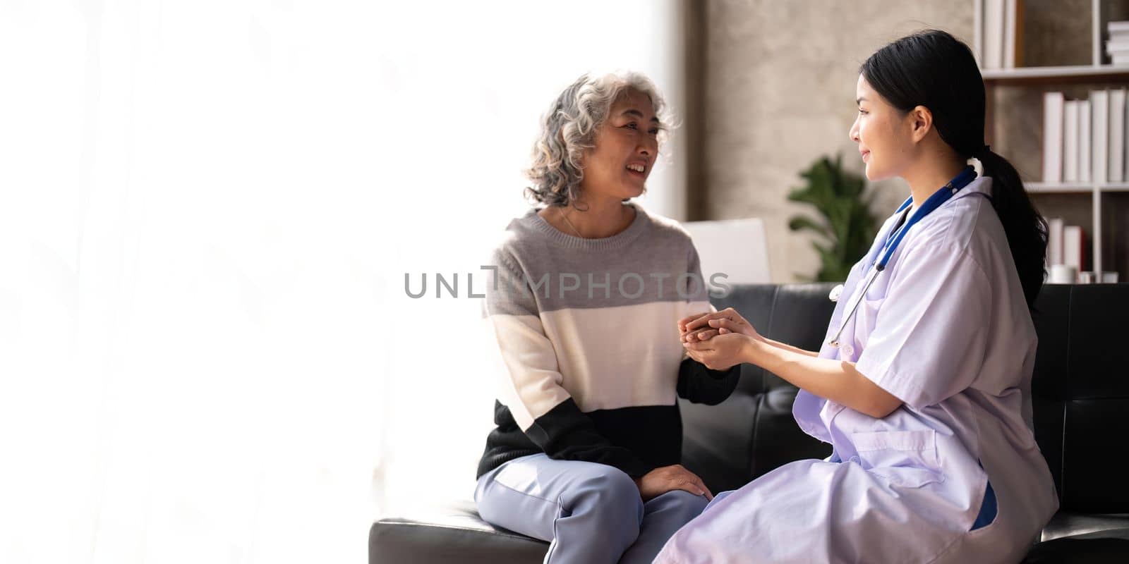 Home caregiver and senior woman holding hands. Professional Elderly Care. Professional care for elderly at nursing homes. Nurse holding hand of senior woman in rest home by nateemee
