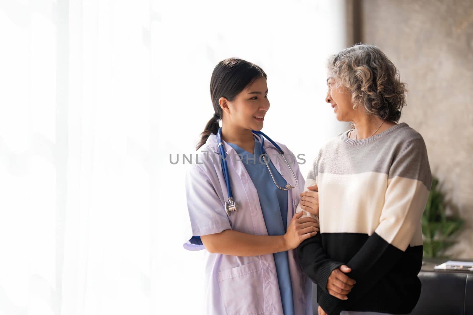 Young caregiver helping senior woman walking. Nurse assisting her old woman patient at nursing home. Senior woman with walking stick being helped by nurse at home. by nateemee