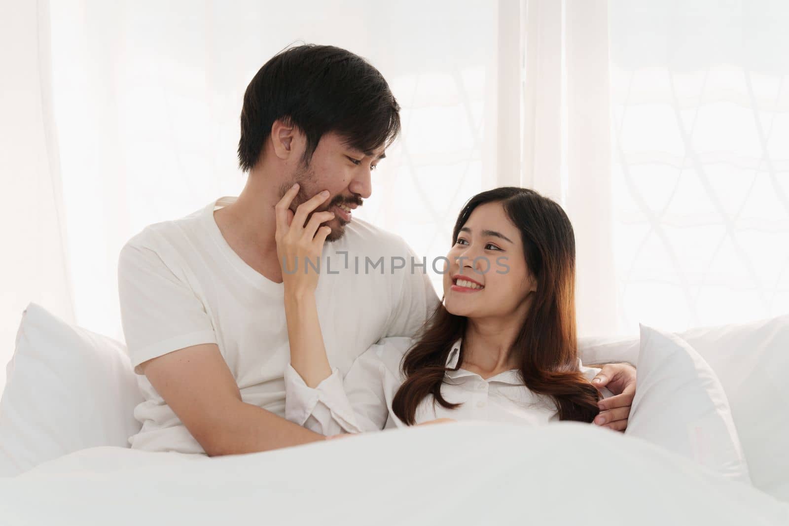 Asian couple lying in bed in a home, anniversary or romance. Intimacy, happy while on romantic vacation, trip by itchaznong