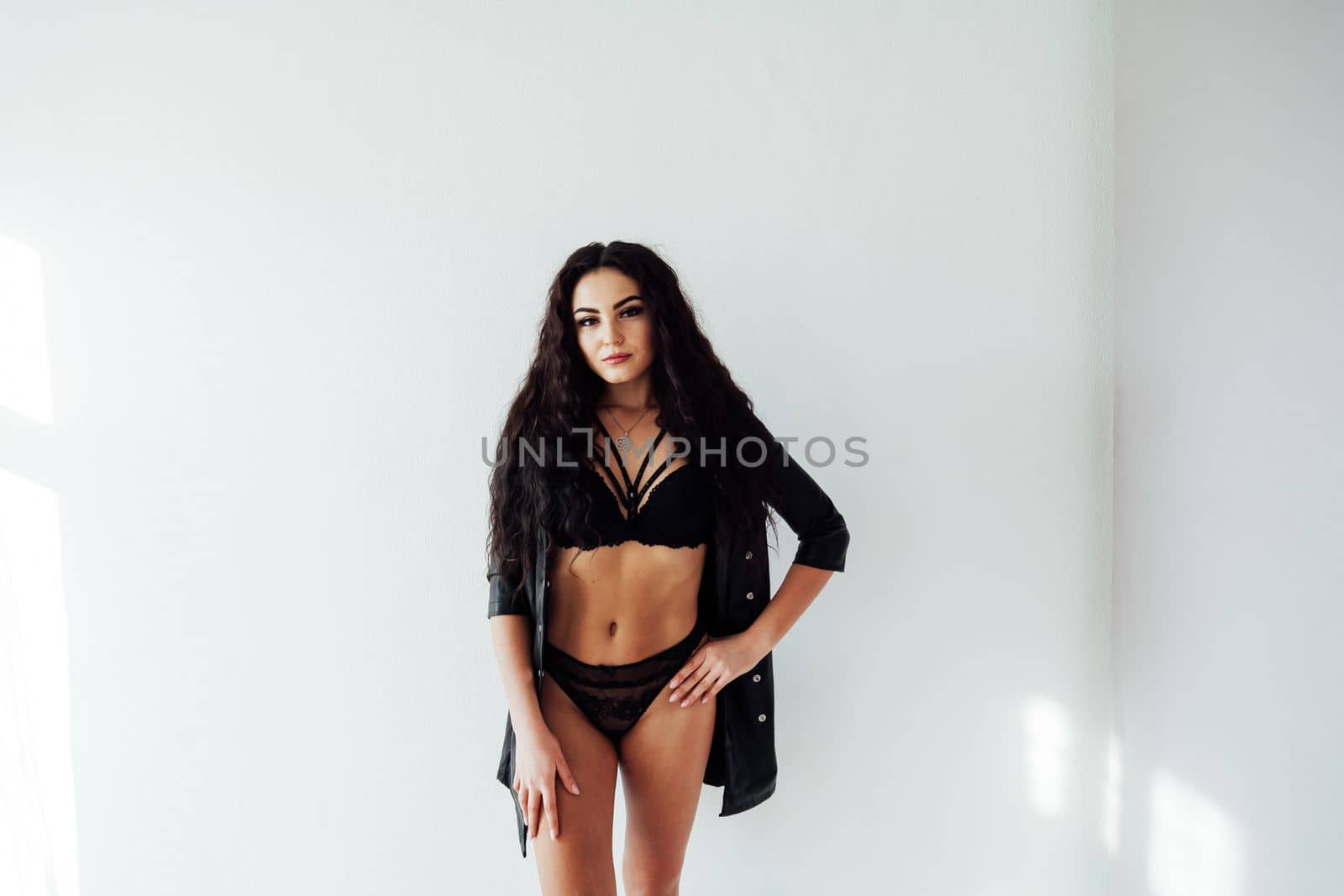 a brunette woman in black underwear stands against a white wall by Simakov