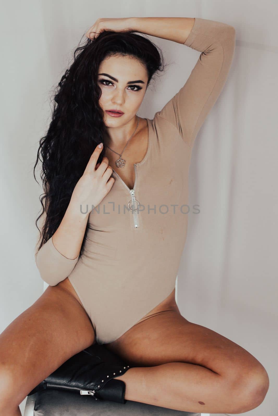 a brunette woman in a beige bodysuit sits on the floor posing by Simakov