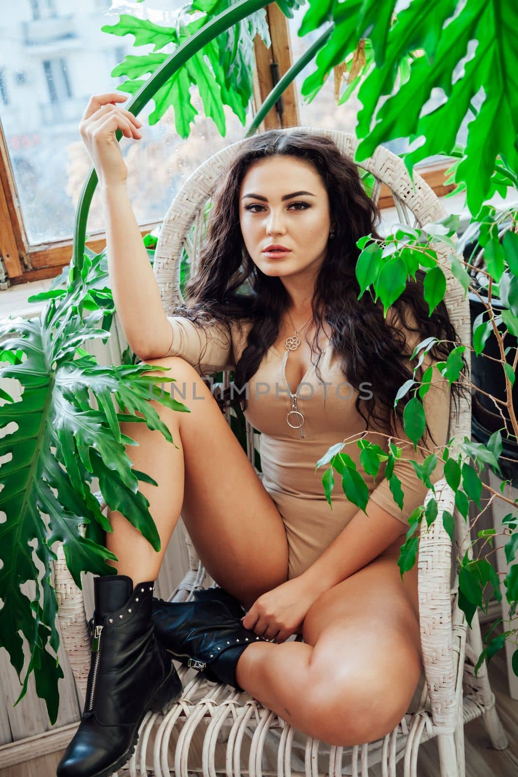 beautiful brunette sits in a chair in a room near green plants by Simakov