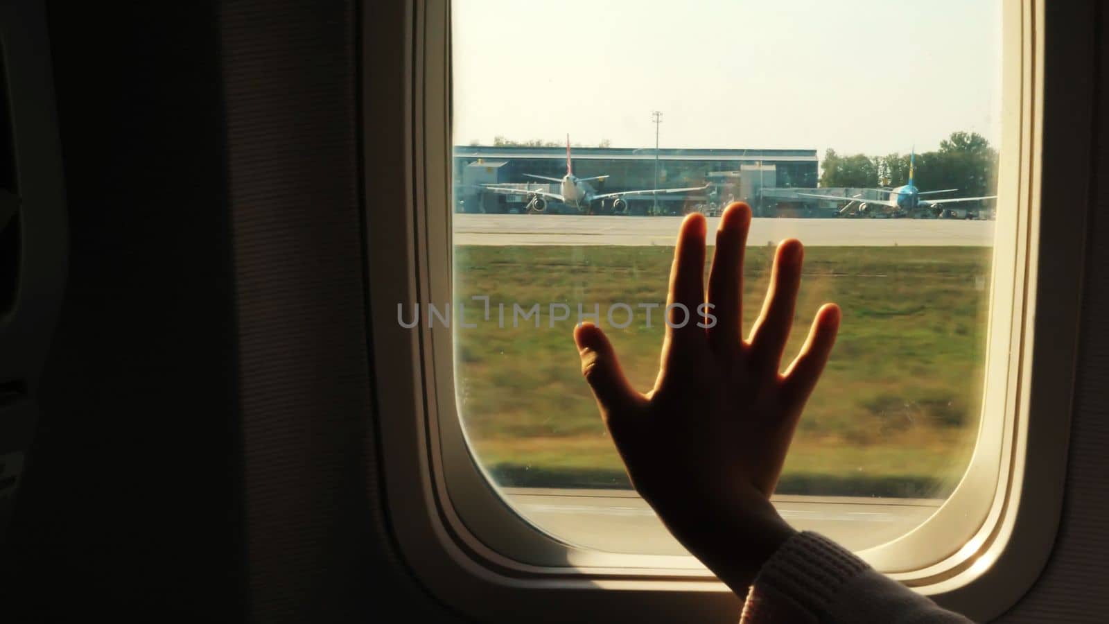 Kid s hand touching airplane window, close up. Silhouette of a child's palm against the background of a window in an airplane. The concept of safety of flights. High quality photo