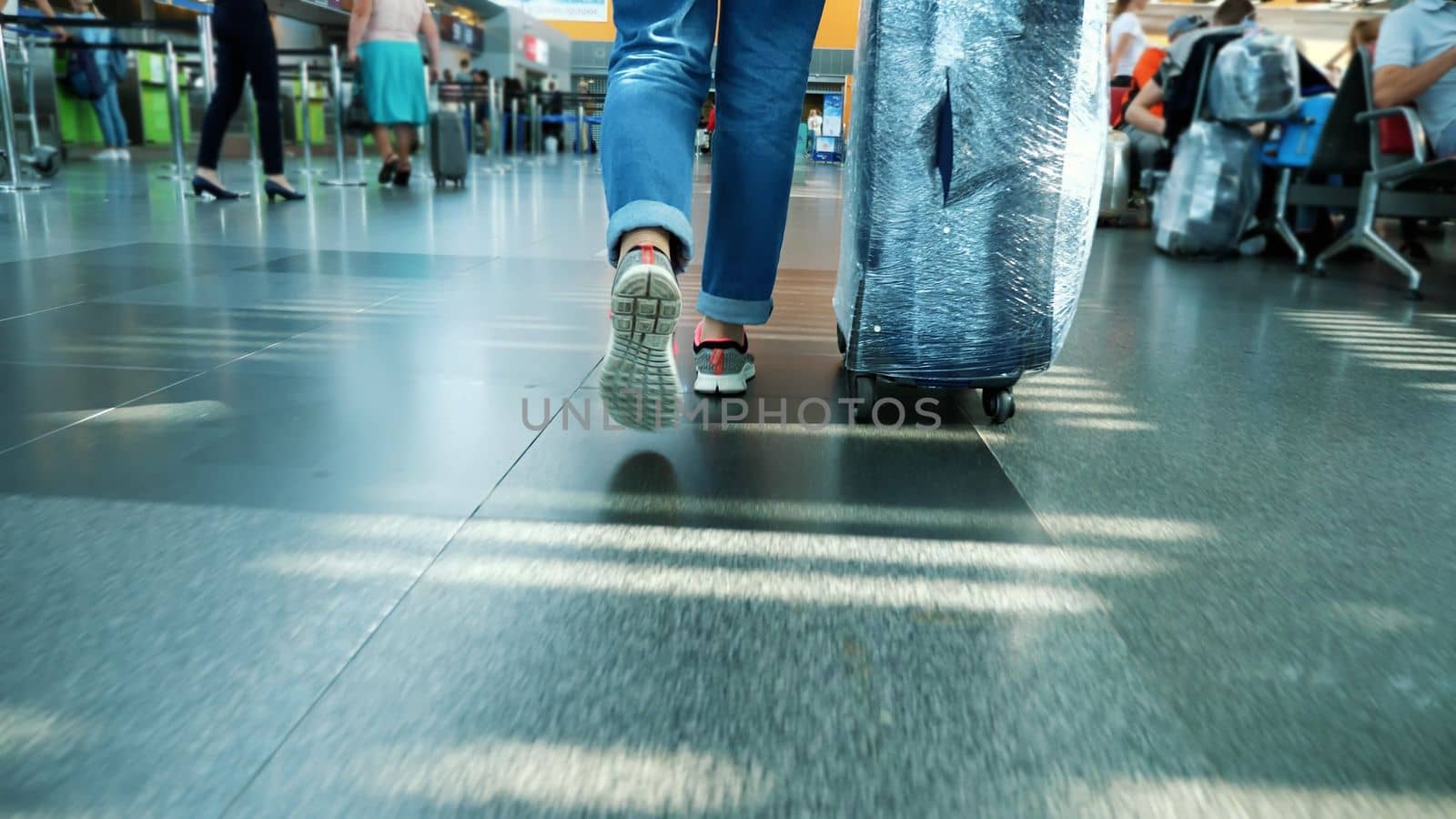 close-up. back view. female legs in sneakers. Woman, Traveler, passenger with her wrapped suitcase, luggage walking through the hall of Airport. High quality photo