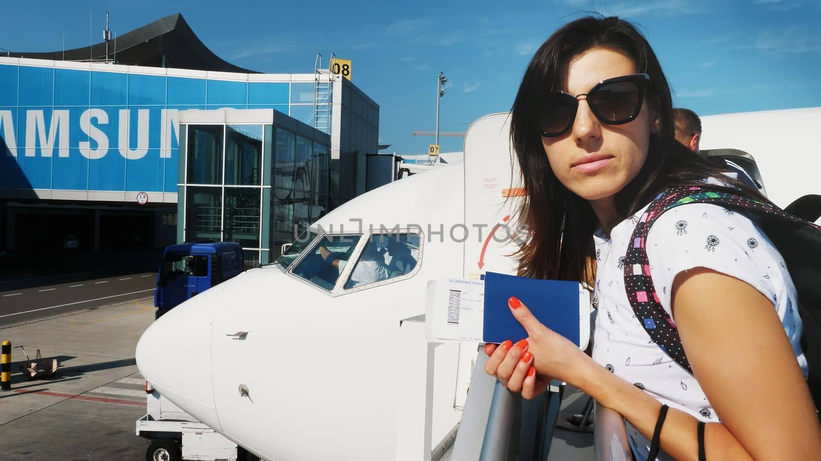 brunette woman in sun glasses, with backpack, holding Airline boarding pass tickets, and passport at airport, on background of the aircraft. summer. High quality photo