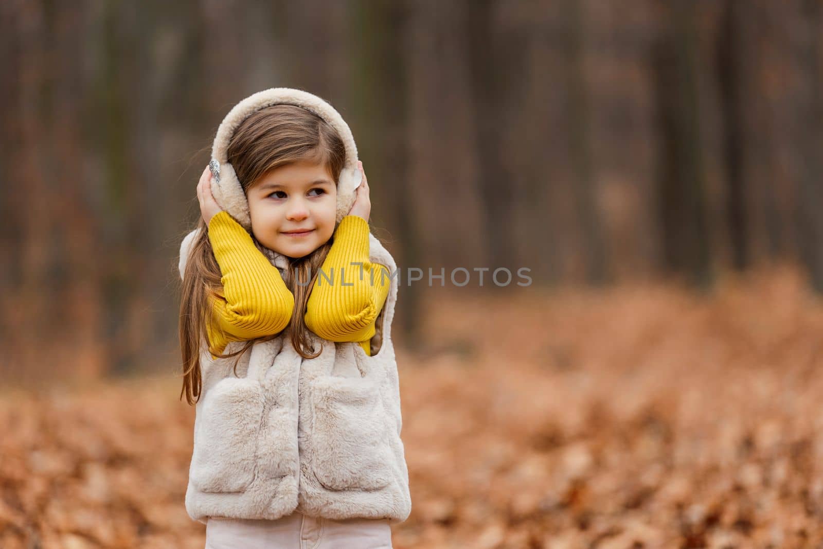 little girl in headphones walks through the autumn forest