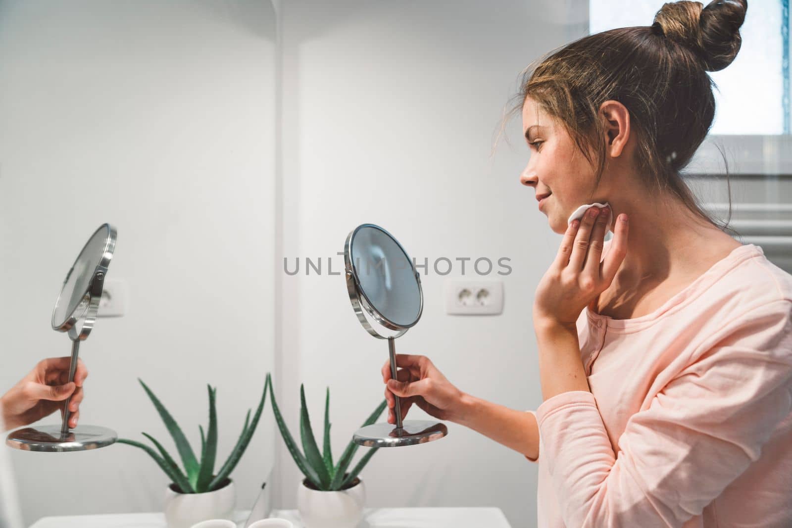Side view of woman cleaning off her make up in the bathroom while looking at herself in the mirror by VisualProductions